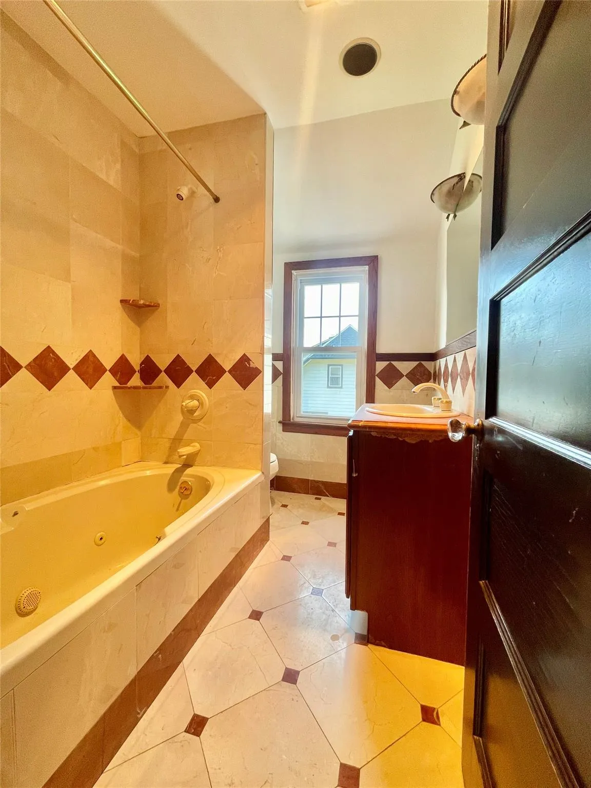 Bathroom with a combined bath / shower with jetted tub, tile walls, vanity, tile patterned floors, and wainscoting Bathroom with a combined bath / shower with jetted tub, tile walls, vanity, tile patterned floors, and wainscoting