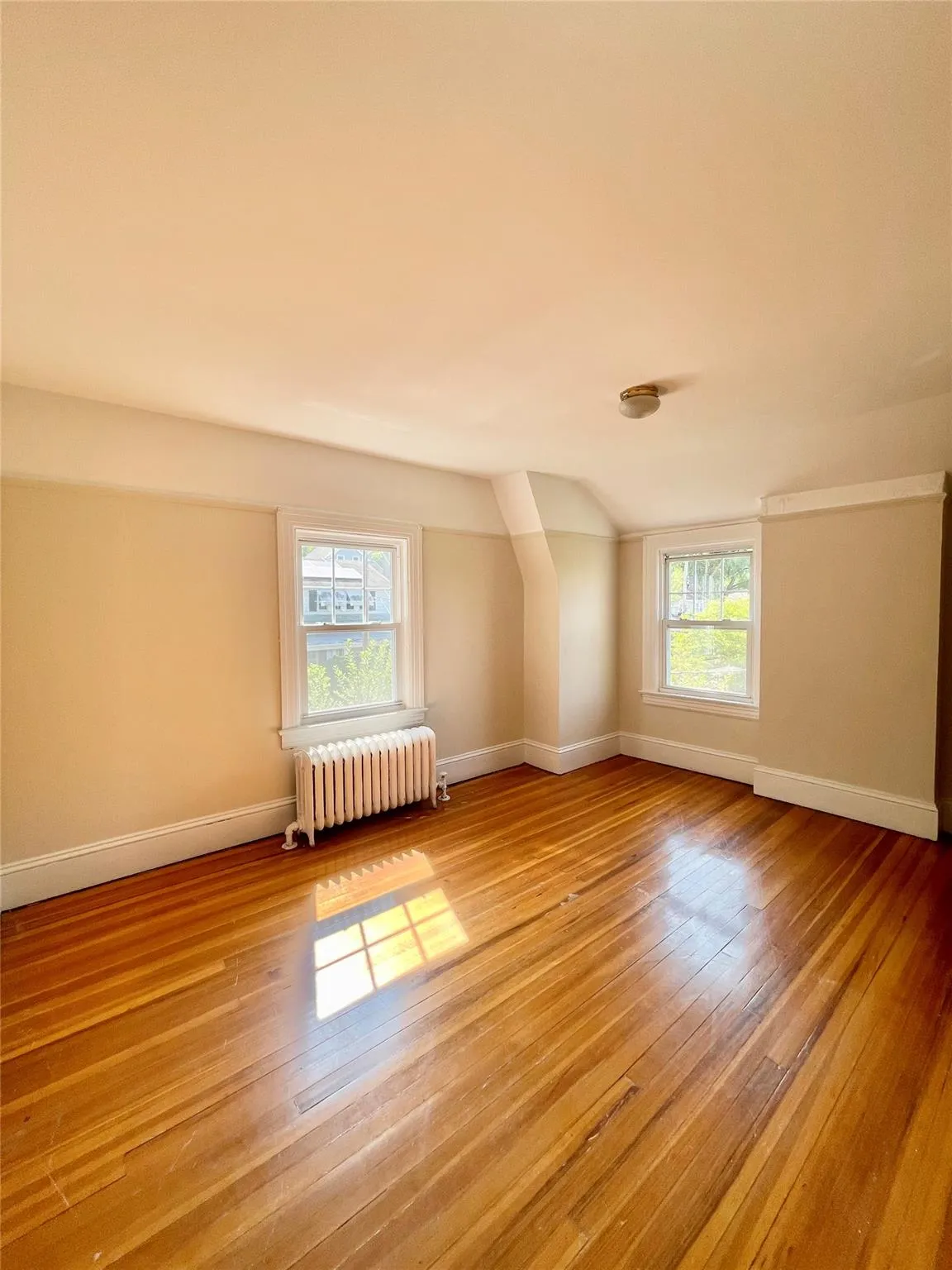 Additional living space with radiator heating unit, light wood-type flooring, plenty of natural light, and vaulted ceiling Additional living space with radiator heating unit, light wood-type flooring, plenty of natural light, and vaulted ceiling