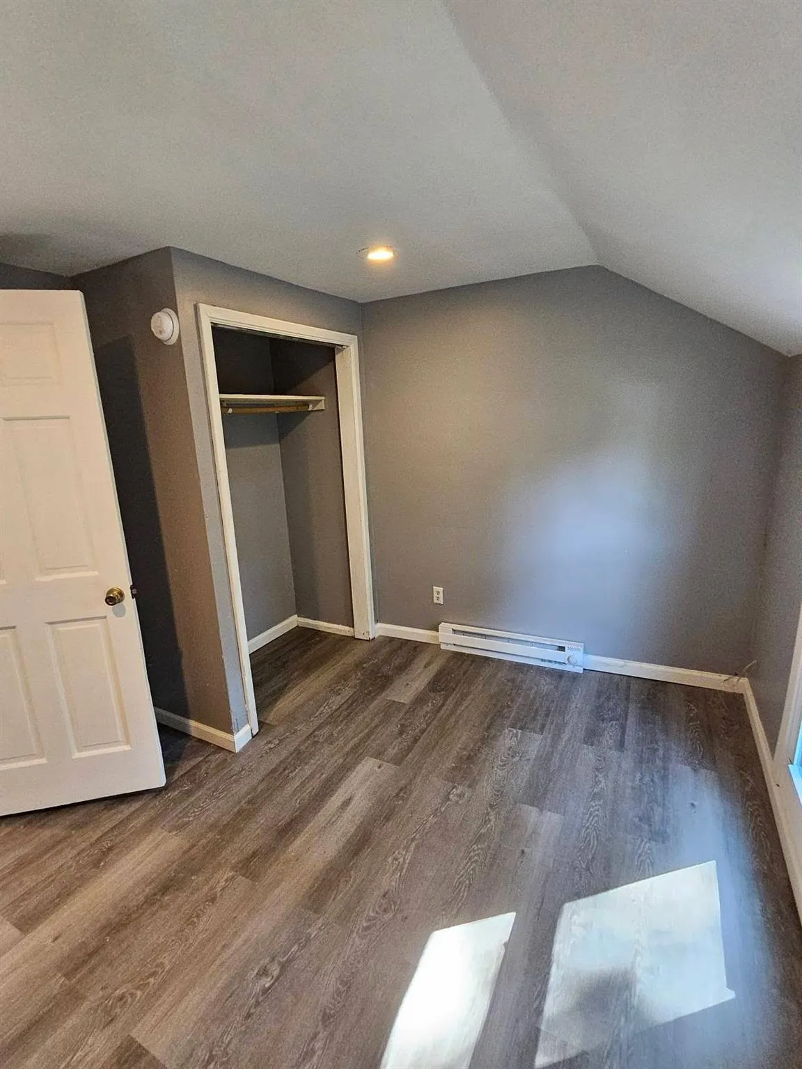 Unfurnished bedroom featuring wood finished floors, a baseboard heating unit, a closet, lofted ceiling, and recessed lighting Unfurnished bedroom featuring wood finished floors, a baseboard heating unit, a closet, lofted ceiling, and recessed lighting