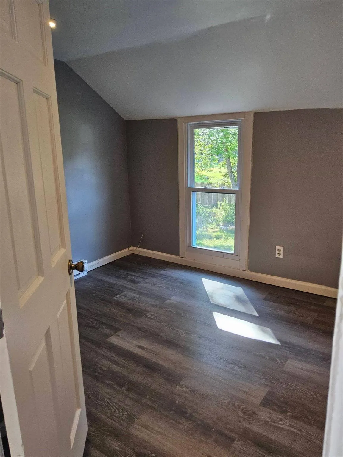 Empty room featuring lofted ceiling and dark wood-style flooring Empty room featuring lofted ceiling and dark wood-style flooring