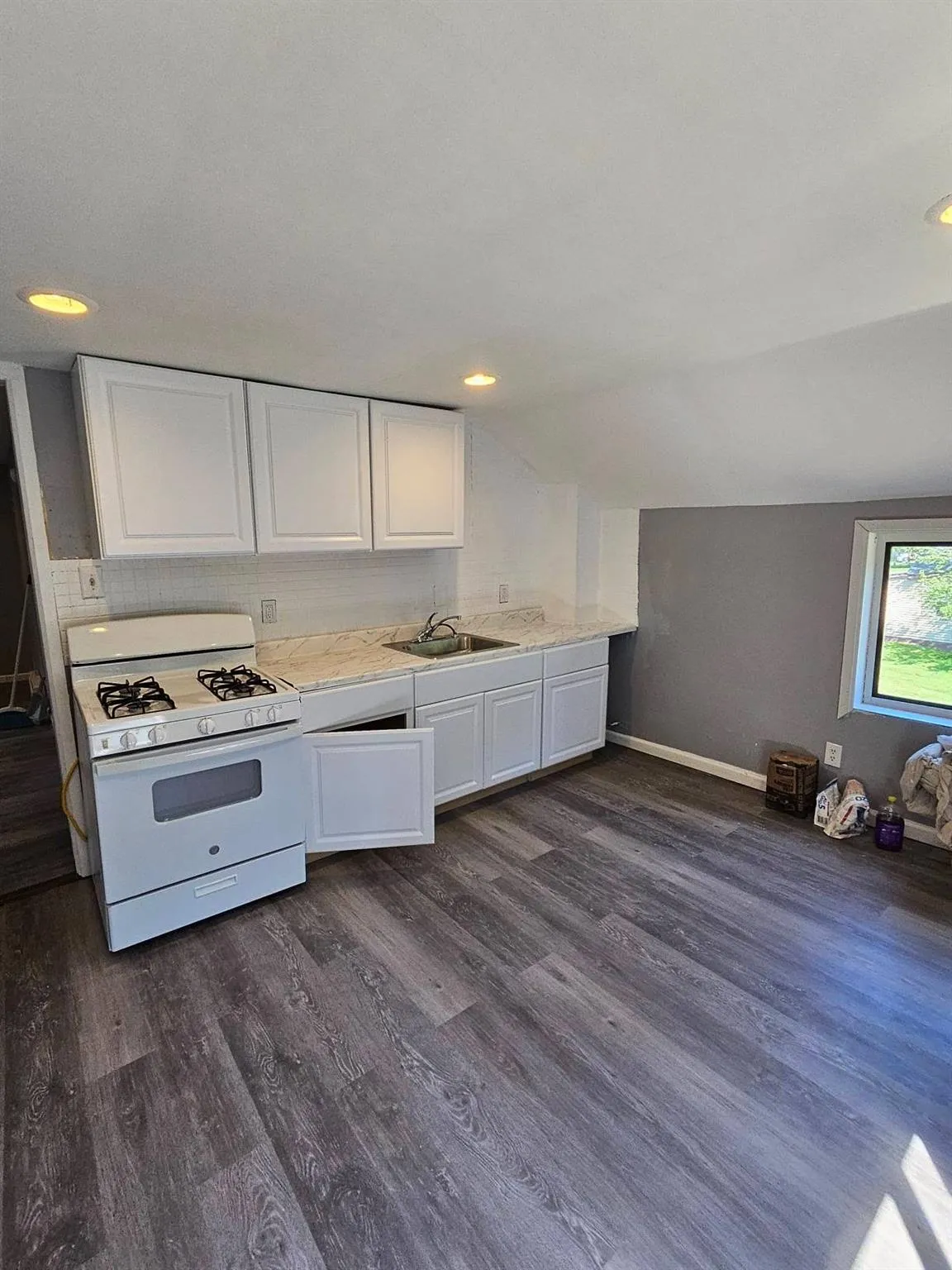 Kitchen with white gas range oven, white cabinets, light countertops, dark wood-style flooring, and vaulted ceiling Kitchen with white gas range oven, white cabinets, light countertops, dark wood-style flooring, and vaulted ceiling