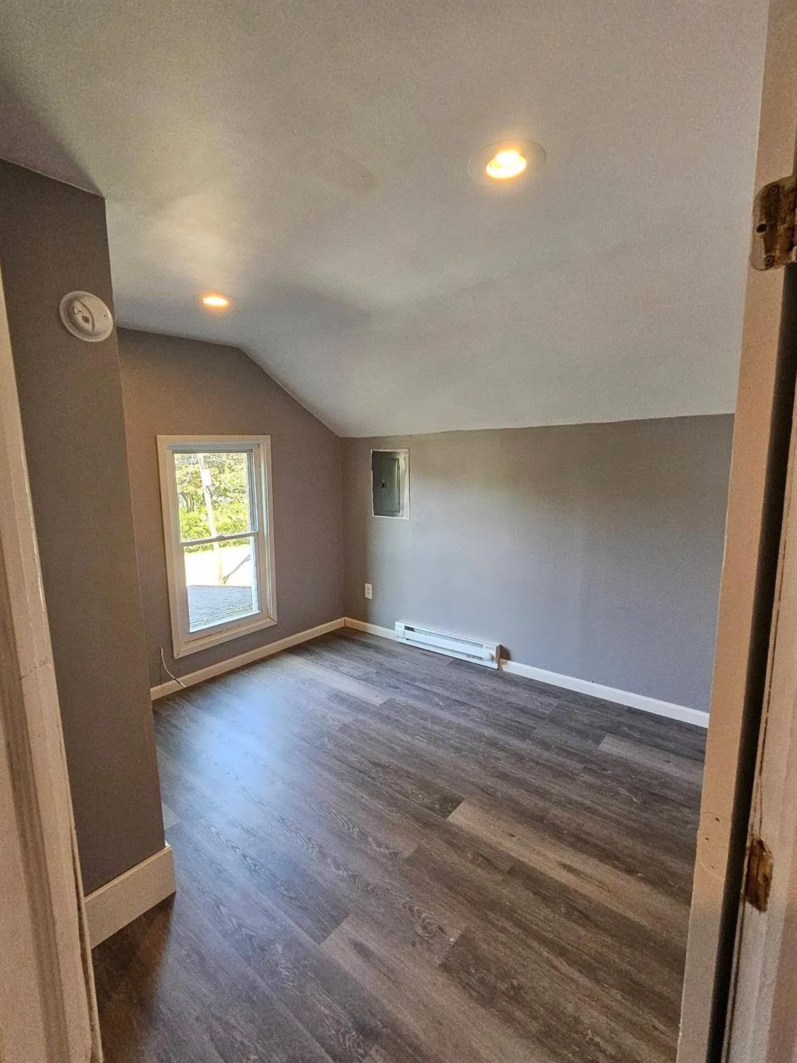 Additional living space with lofted ceiling, dark wood-type flooring, baseboard heating, a textured ceiling, and electric panel Additional living space with lofted ceiling, dark wood-type flooring, baseboard heating, a textured ceiling, and electric panel