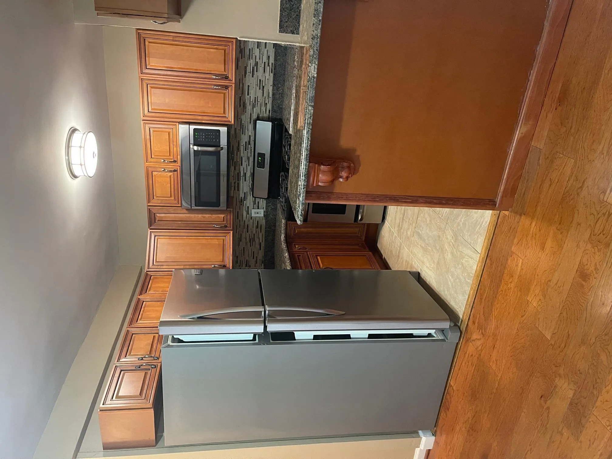 Kitchen with fridge, stove, backsplash, light wood-style floors, and brown cabinetry Kitchen with fridge, stove, backsplash, light wood-style floors, and brown cabinetry