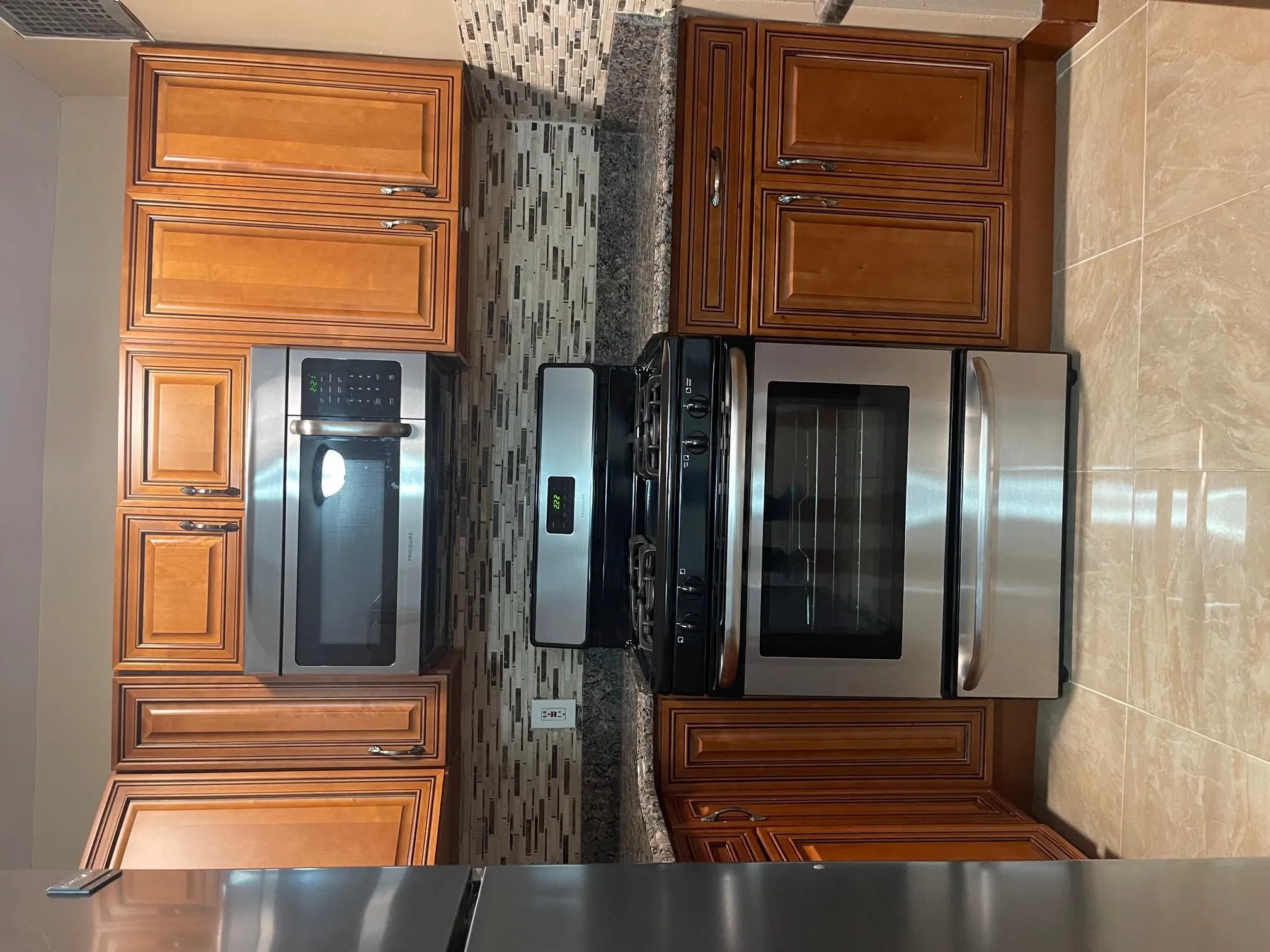 Kitchen featuring stainless steel range with gas cooktop, decorative backsplash, dark countertops, fridge, and brown cabinets Kitchen featuring stainless steel range with gas cooktop, decorative backsplash, dark countertops, fridge, and brown cabinets