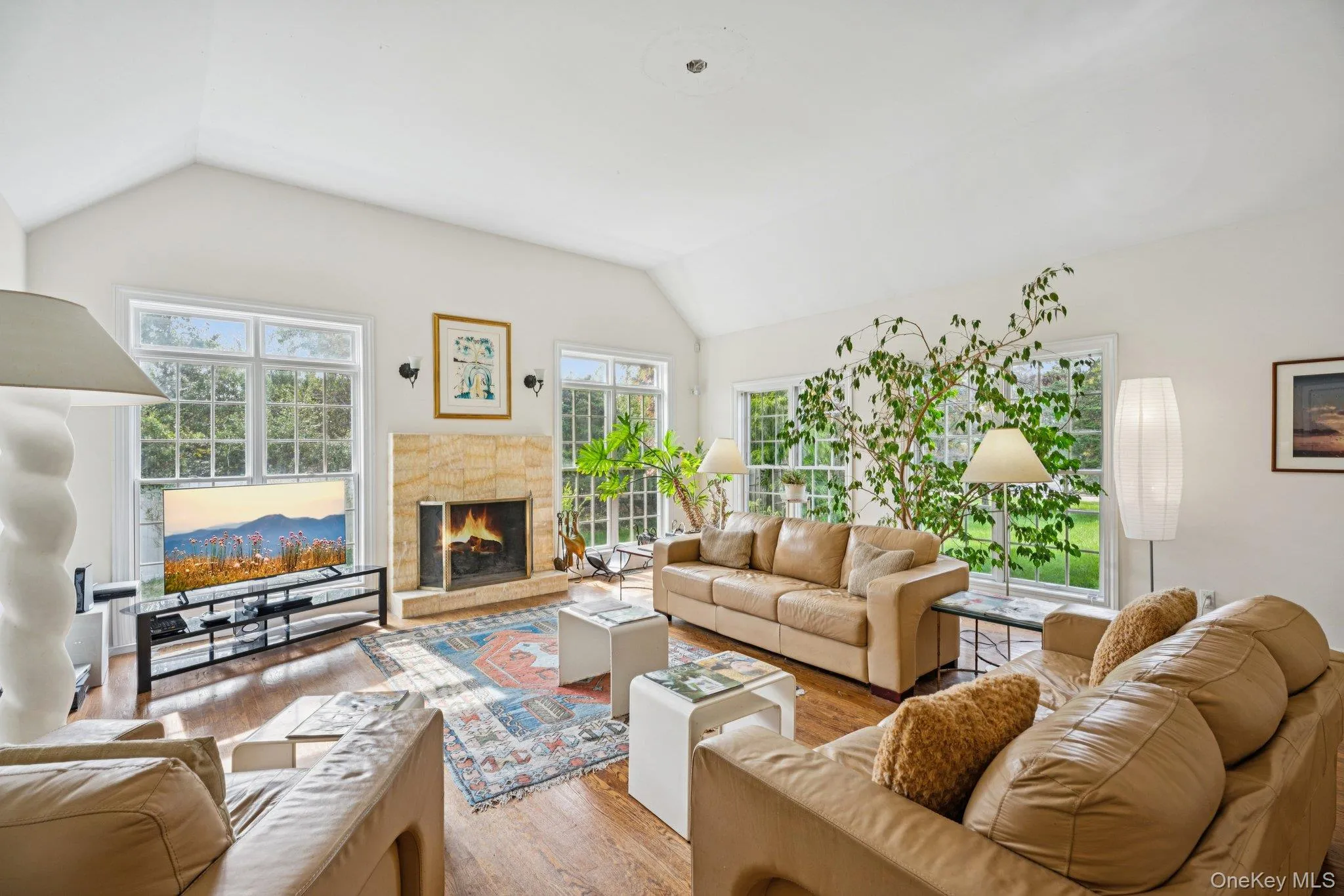 An exquisite living area showcasing vaulted ceilings, rich oak hardwood floors, and a timeless wood-burning fireplace, beautifully encased in floor-to-ceiling windows and sleek glass sliders that invite an abundance of natural light. An exquisite living area showcasing vaulted ceilings, rich oak hardwood floors, and a timeless wood-burning fireplace, beautifully encased in floor-to-ceiling windows and sleek glass sliders that invite an abundance of natural light.