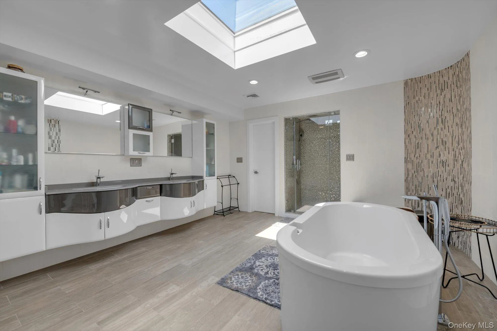 Primary bath with a skylight, double vanity, a freestanding bath, a shower stall, and woodlike finished floors Primary bath with a skylight, double vanity, a freestanding bath, a shower stall, and woodlike finished floors