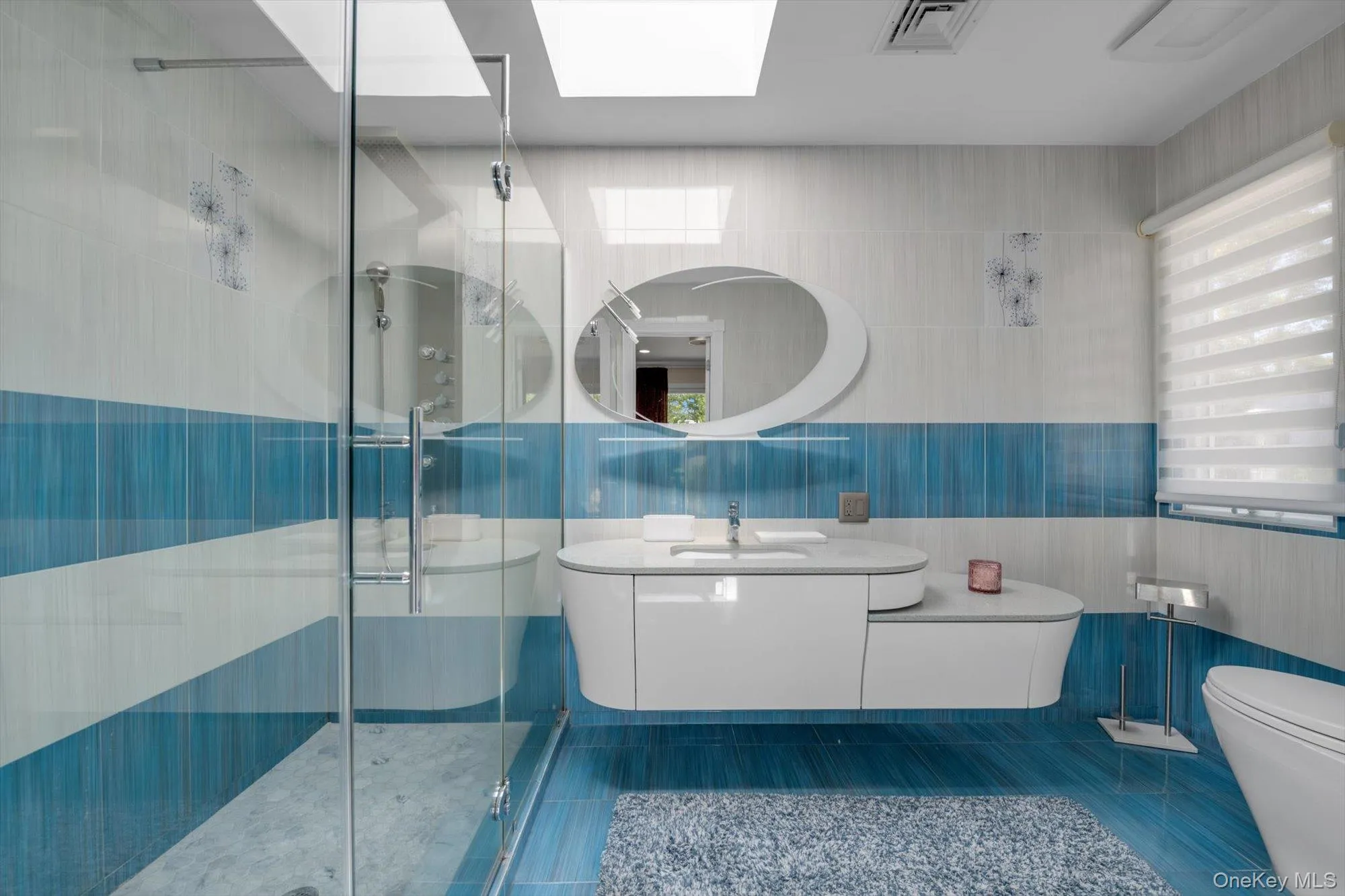 Bathroom featuring tile walls, a shower stall, vanity, tile patterned floors, and a skylight Bathroom featuring tile walls, a shower stall, vanity, tile patterned floors, and a skylight