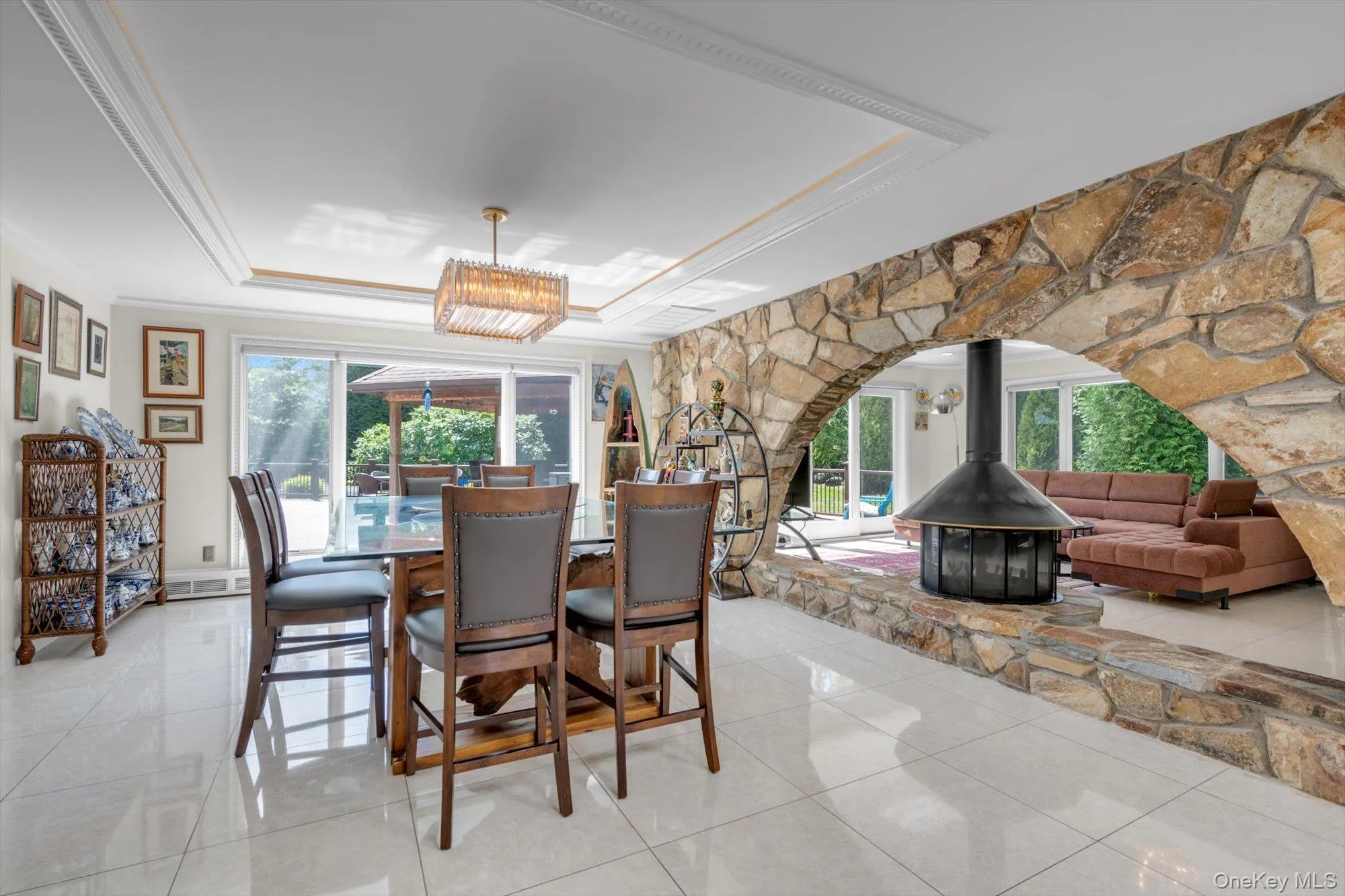 Dining Room with a raised ceiling, a wood burning fireplace, ornamental molding, light tile patterned floors, and a chandelier Dining Room with a raised ceiling, a wood burning fireplace, ornamental molding, light tile patterned floors, and a chandelier