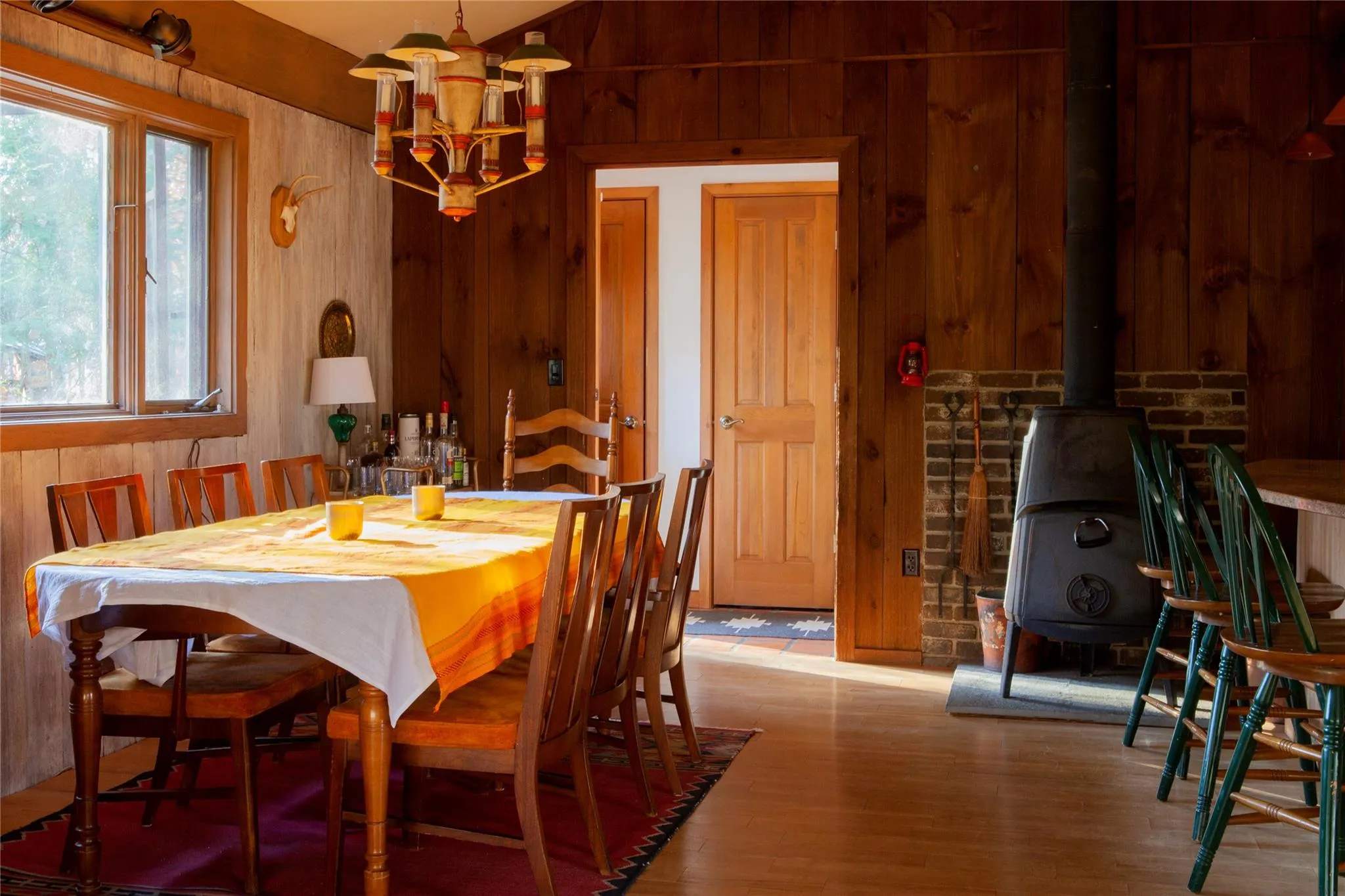 Dining area featuring wooden walls, a wood stove, vaulted ceiling, wood finished floors, and a chandelier Dining area featuring wooden walls, a wood stove, vaulted ceiling, wood finished floors, and a chandelier