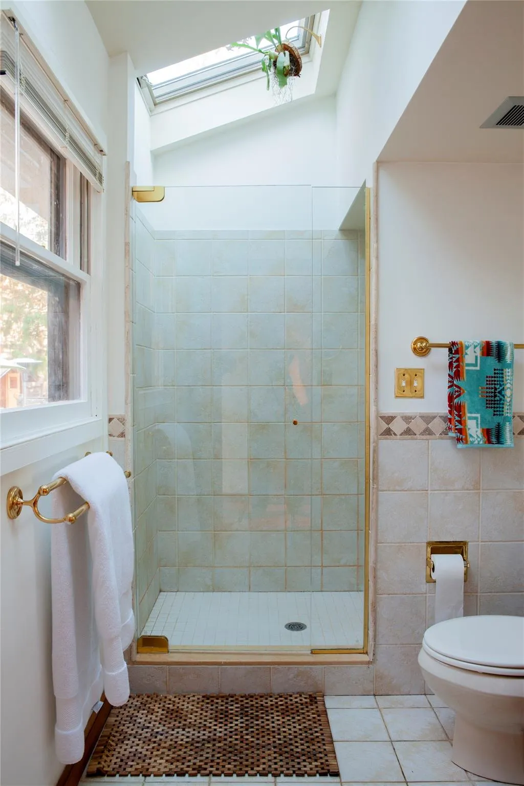 Full bathroom with a shower stall, tile walls, a skylight, tile patterned flooring, and a wainscoted wall Full bathroom with a shower stall, tile walls, a skylight, tile patterned flooring, and a wainscoted wall
