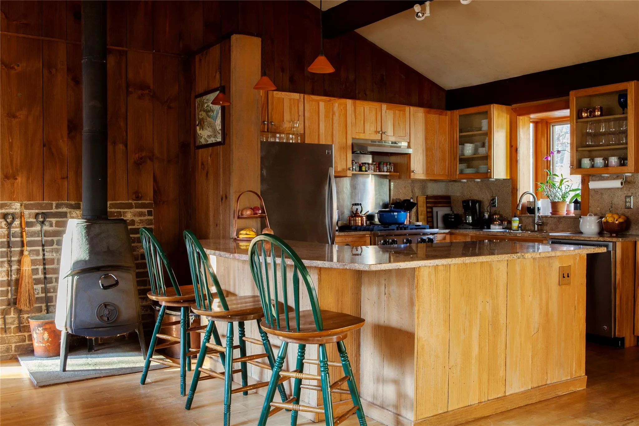 Kitchen with freestanding refrigerator, a wood stove, light wood finished floors, wooden walls, and dishwasher Kitchen with freestanding refrigerator, a wood stove, light wood finished floors, wooden walls, and dishwasher