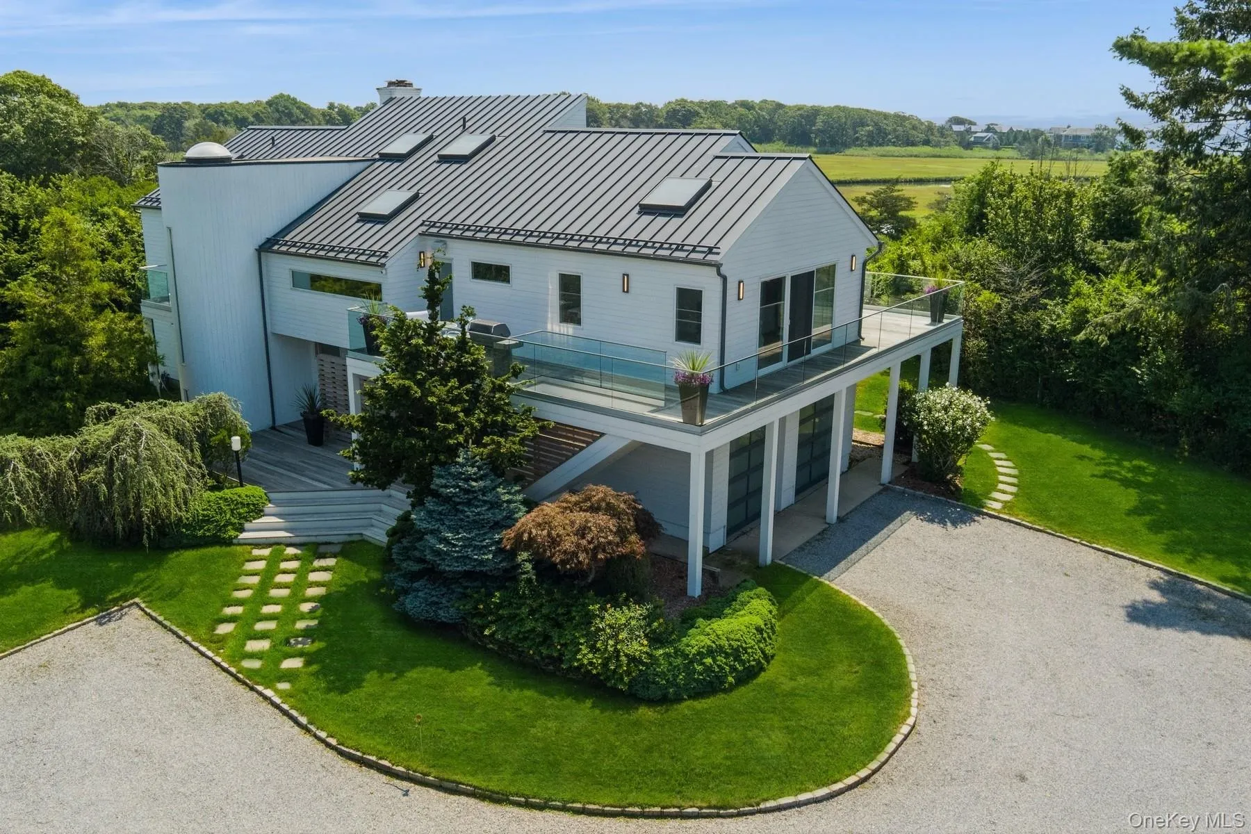 Rear view of property featuring a standing seam roof, a balcony, gravel driveway, a metal roof, and a lawn Rear view of property featuring a standing seam roof, a balcony, gravel driveway, a metal roof, and a lawn