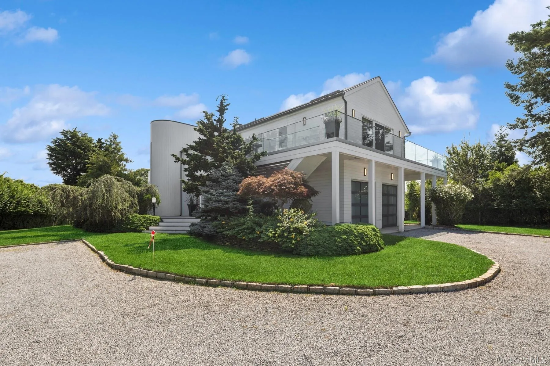 Back of property featuring a balcony, a lawn, and gravel driveway Back of property featuring a balcony, a lawn, and gravel driveway