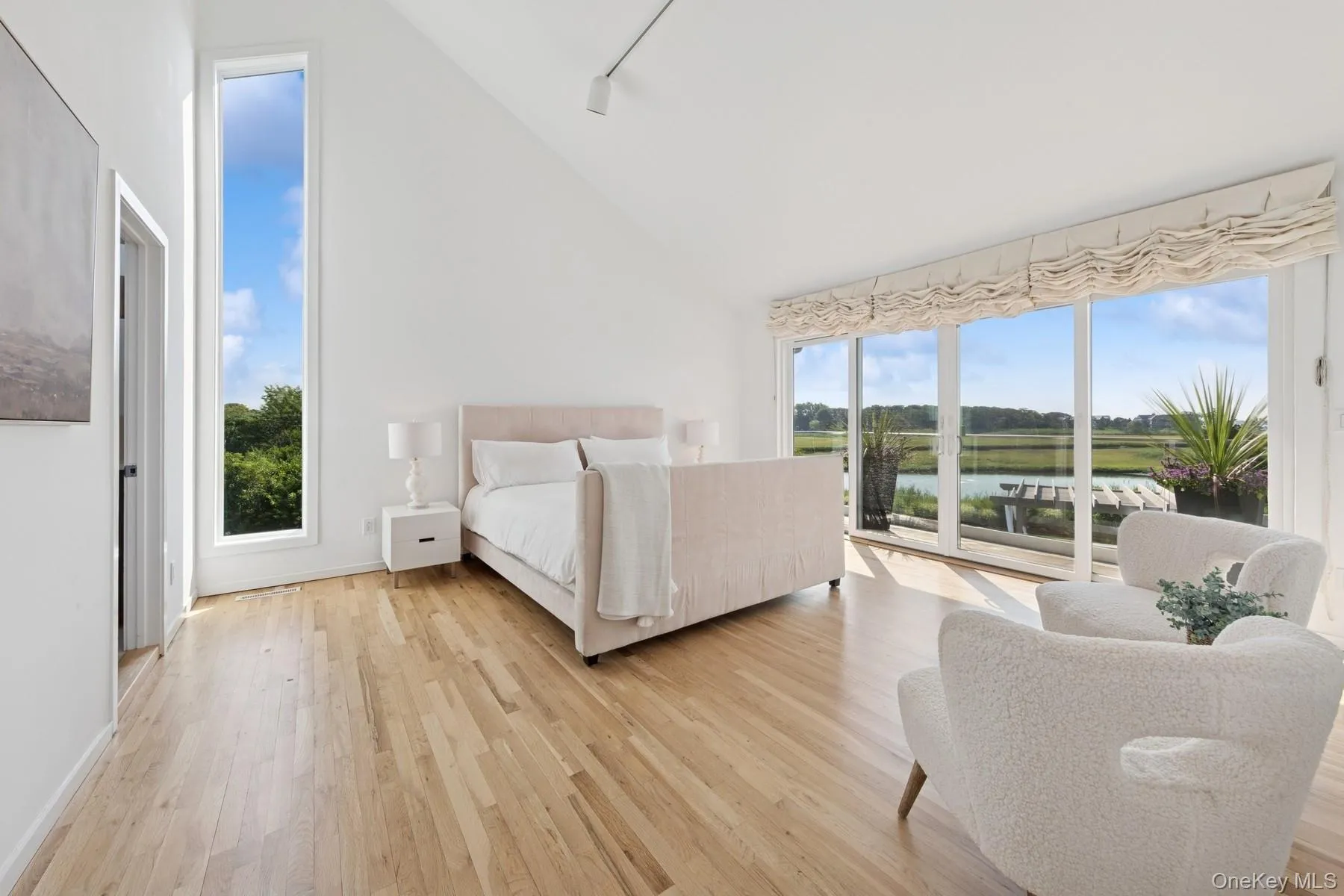 Bedroom featuring access to exterior, high vaulted ceiling, light wood-style flooring, track lighting, and a water view Bedroom featuring access to exterior, high vaulted ceiling, light wood-style flooring, track lighting, and a water view