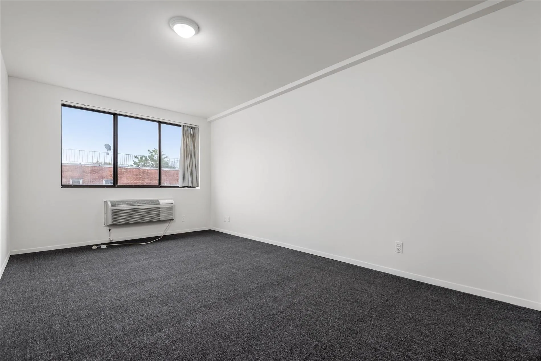 Empty room featuring dark carpet and a wall mounted air conditioner Empty room featuring dark carpet and a wall mounted air conditioner