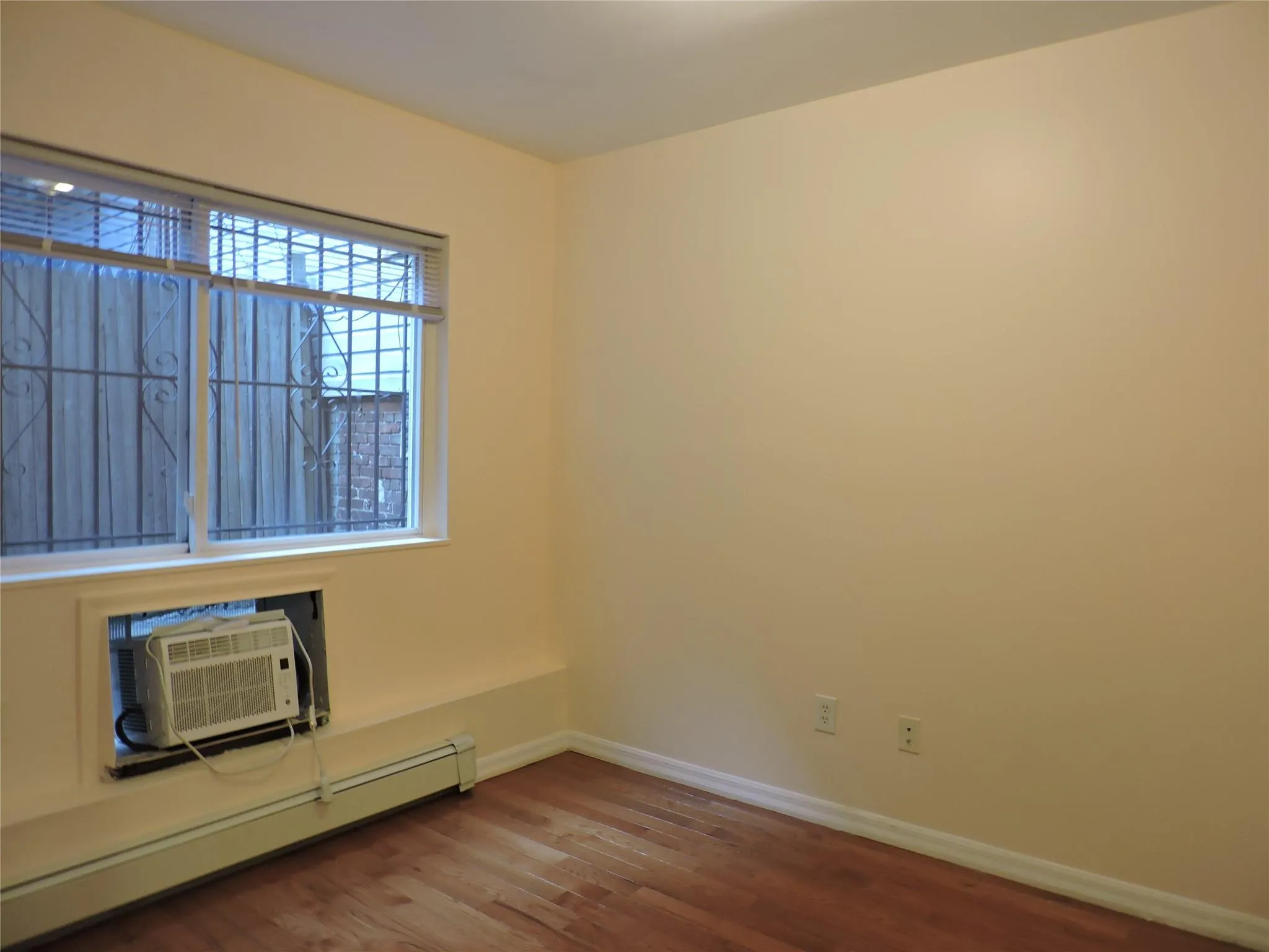 Unfurnished room featuring a baseboard radiator, wood finished floors, and an AC wall unit Unfurnished room featuring a baseboard radiator, wood finished floors, and an AC wall unit