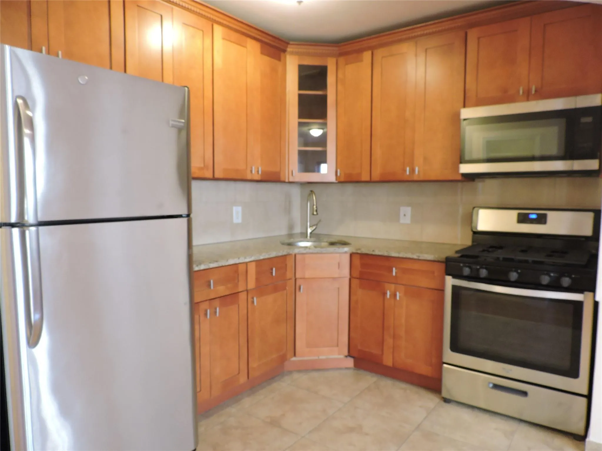 Kitchen with appliances with stainless steel finishes, light stone countertops, glass insert cabinets, and light tile patterned flooring Kitchen with appliances with stainless steel finishes, light stone countertops, glass insert cabinets, and light tile patterned flooring