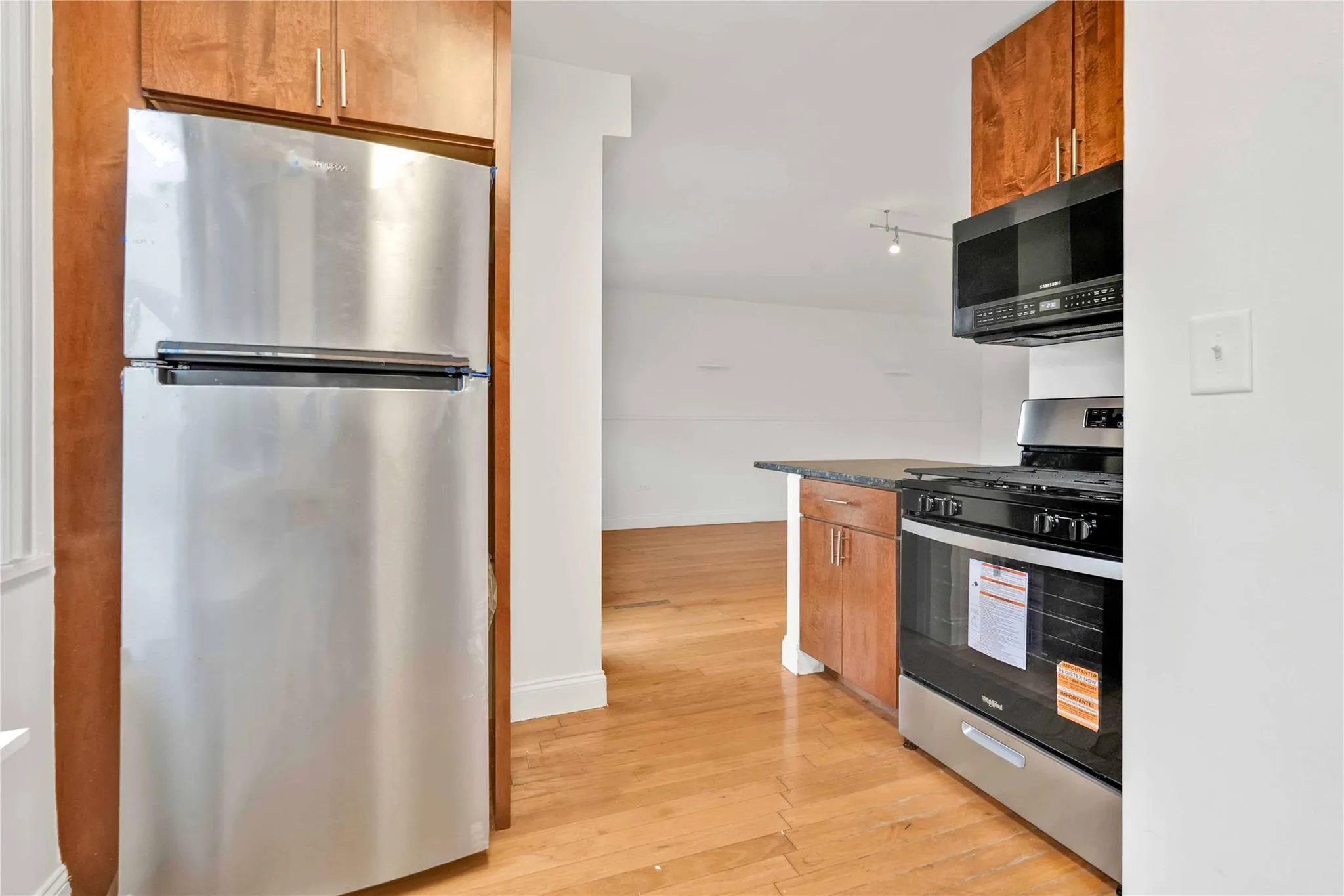 Kitchen with appliances with stainless steel finishes, light wood-style flooring, brown cabinetry, and dark countertops Kitchen with appliances with stainless steel finishes, light wood-style flooring, brown cabinetry, and dark countertops
