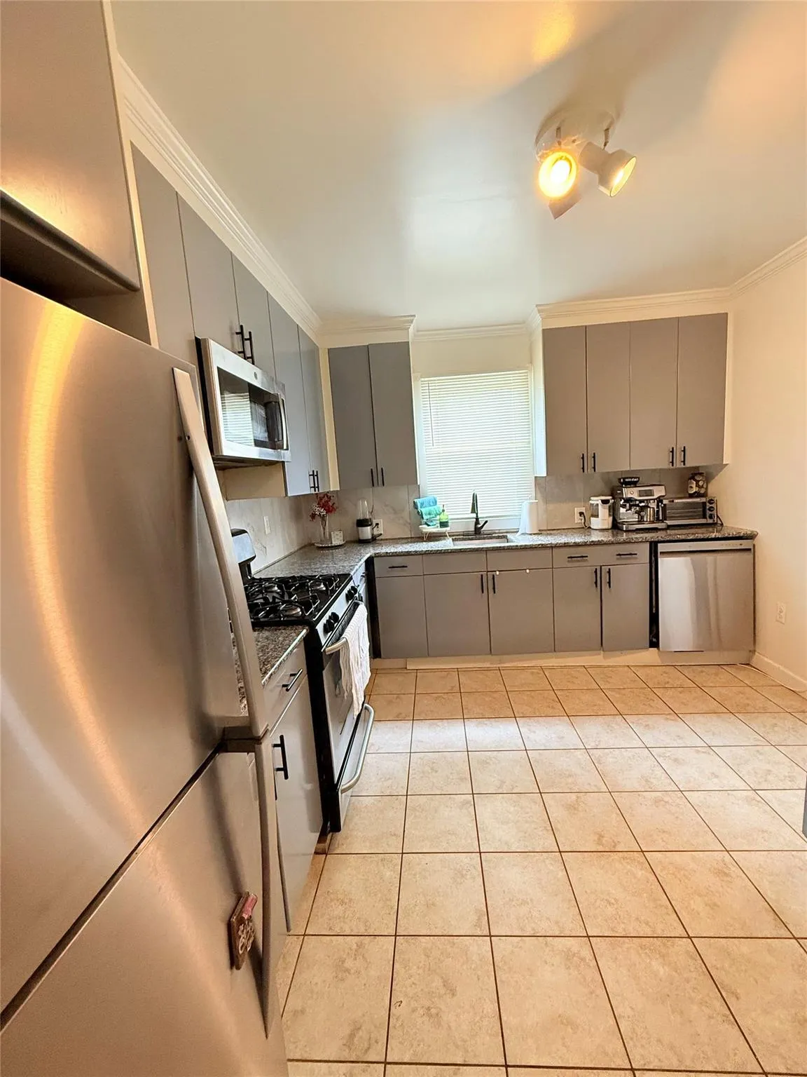Kitchen with gray cabinets, stainless steel appliances, ornamental molding, light tile patterned floors, and tasteful backsplash Kitchen with gray cabinets, stainless steel appliances, ornamental molding, light tile patterned floors, and tasteful backsplash