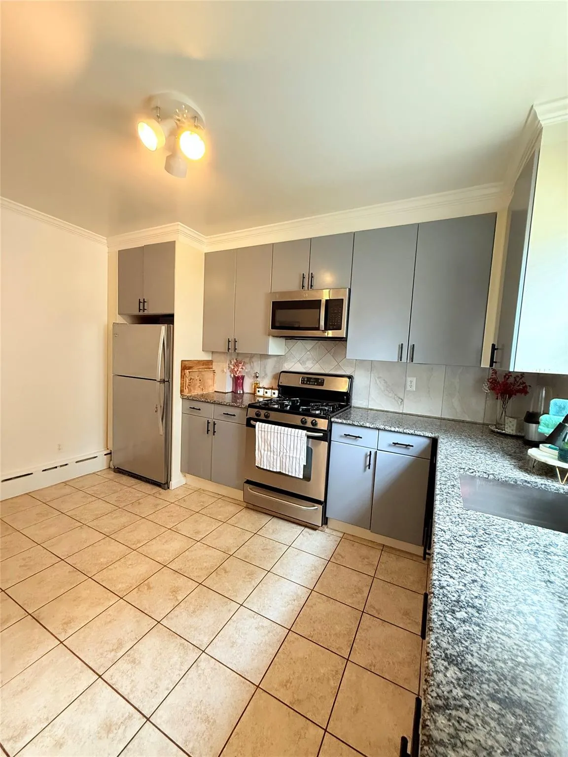 Kitchen featuring gray cabinetry, crown molding, backsplash, appliances with stainless steel finishes, and baseboard heating Kitchen featuring gray cabinetry, crown molding, backsplash, appliances with stainless steel finishes, and baseboard heating
