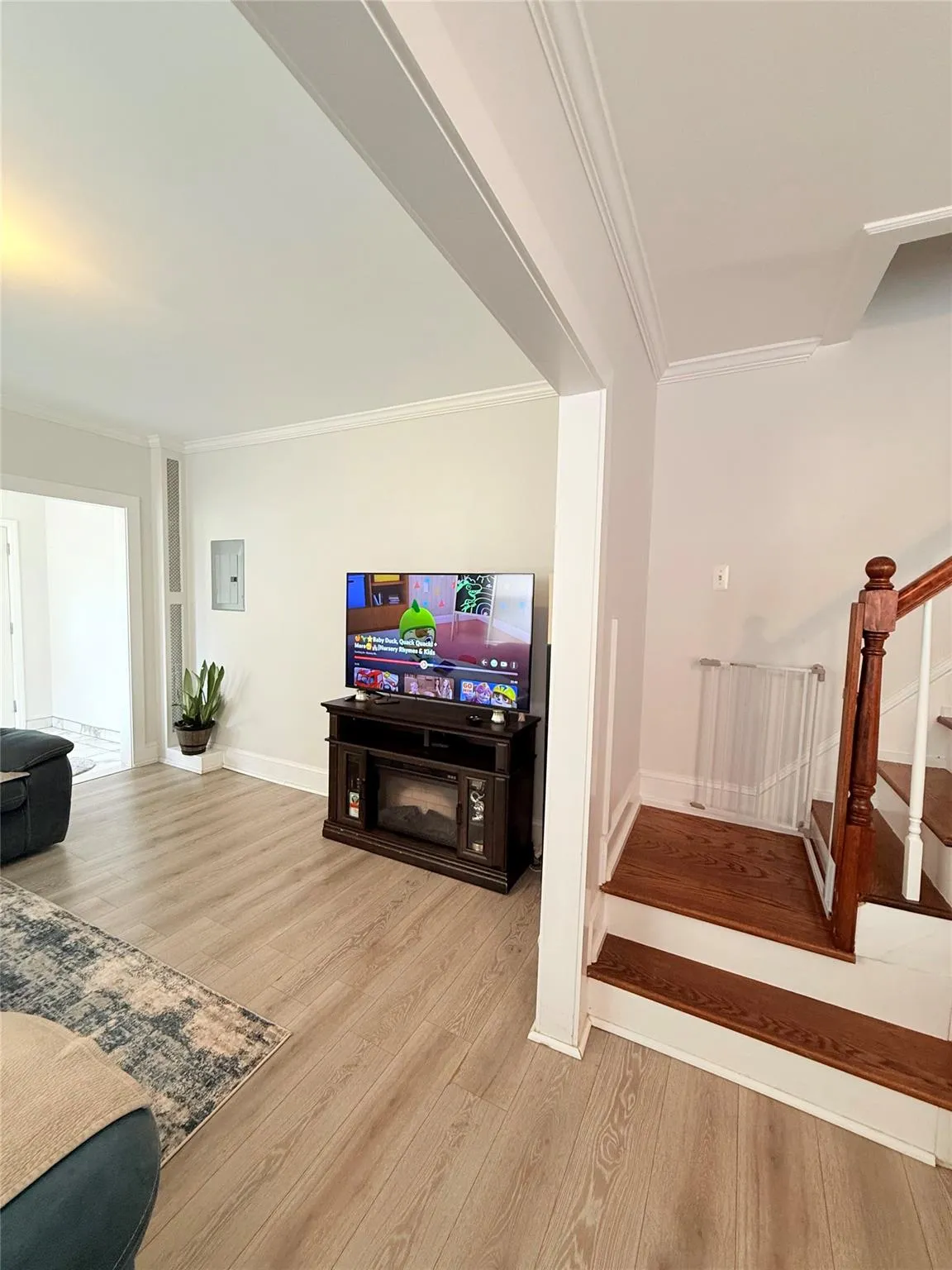 Living area with light wood finished floors, ornamental molding, stairs, and electric panel Living area with light wood finished floors, ornamental molding, stairs, and electric panel