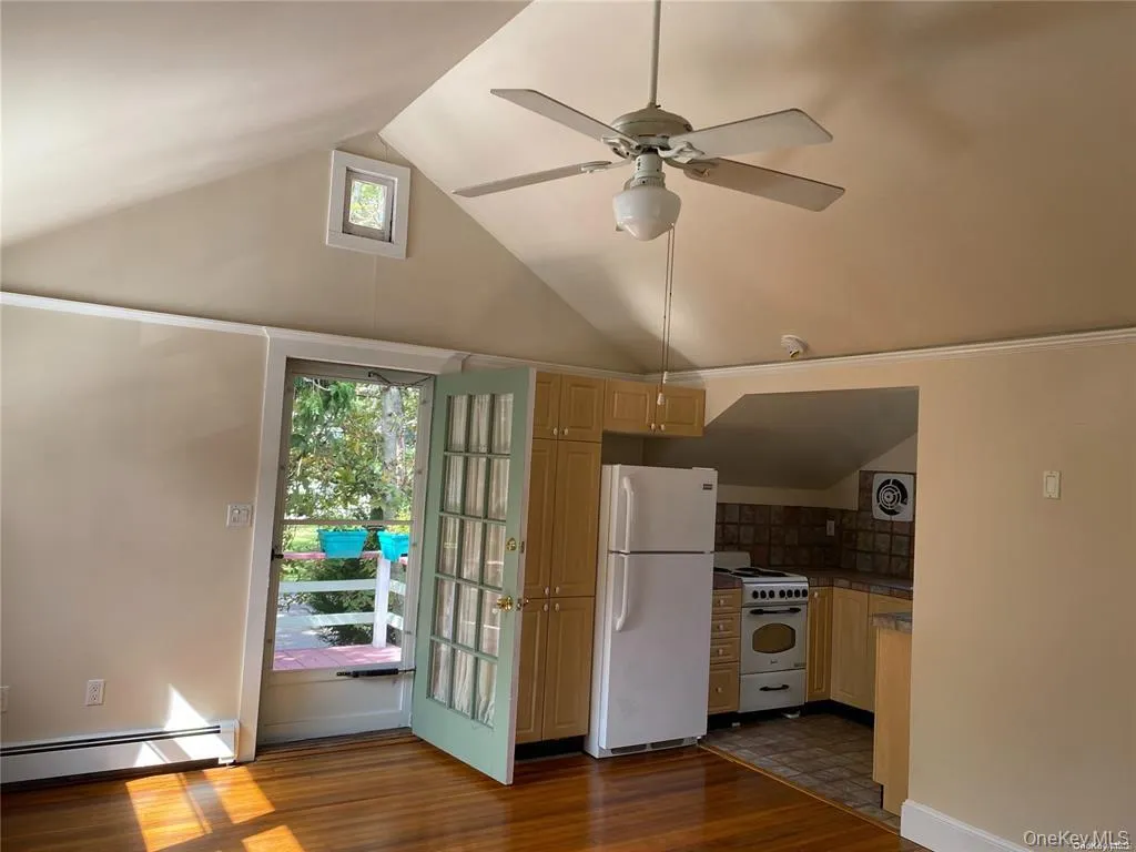 Kitchen with white appliances, vaulted ceiling, a baseboard heating unit, dark wood-type flooring, and a ceiling fan Kitchen with white appliances, vaulted ceiling, a baseboard heating unit, dark wood-type flooring, and a ceiling fan