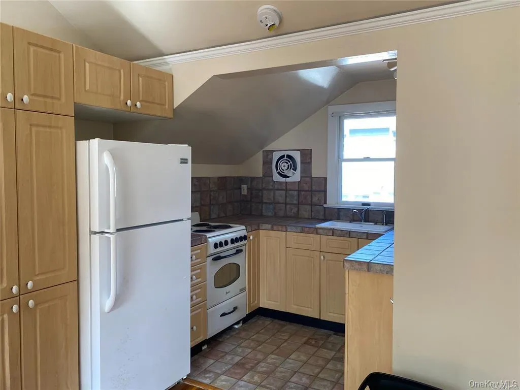 Kitchen with white appliances, light brown cabinetry, backsplash, vaulted ceiling, and ornamental molding Kitchen with white appliances, light brown cabinetry, backsplash, vaulted ceiling, and ornamental molding