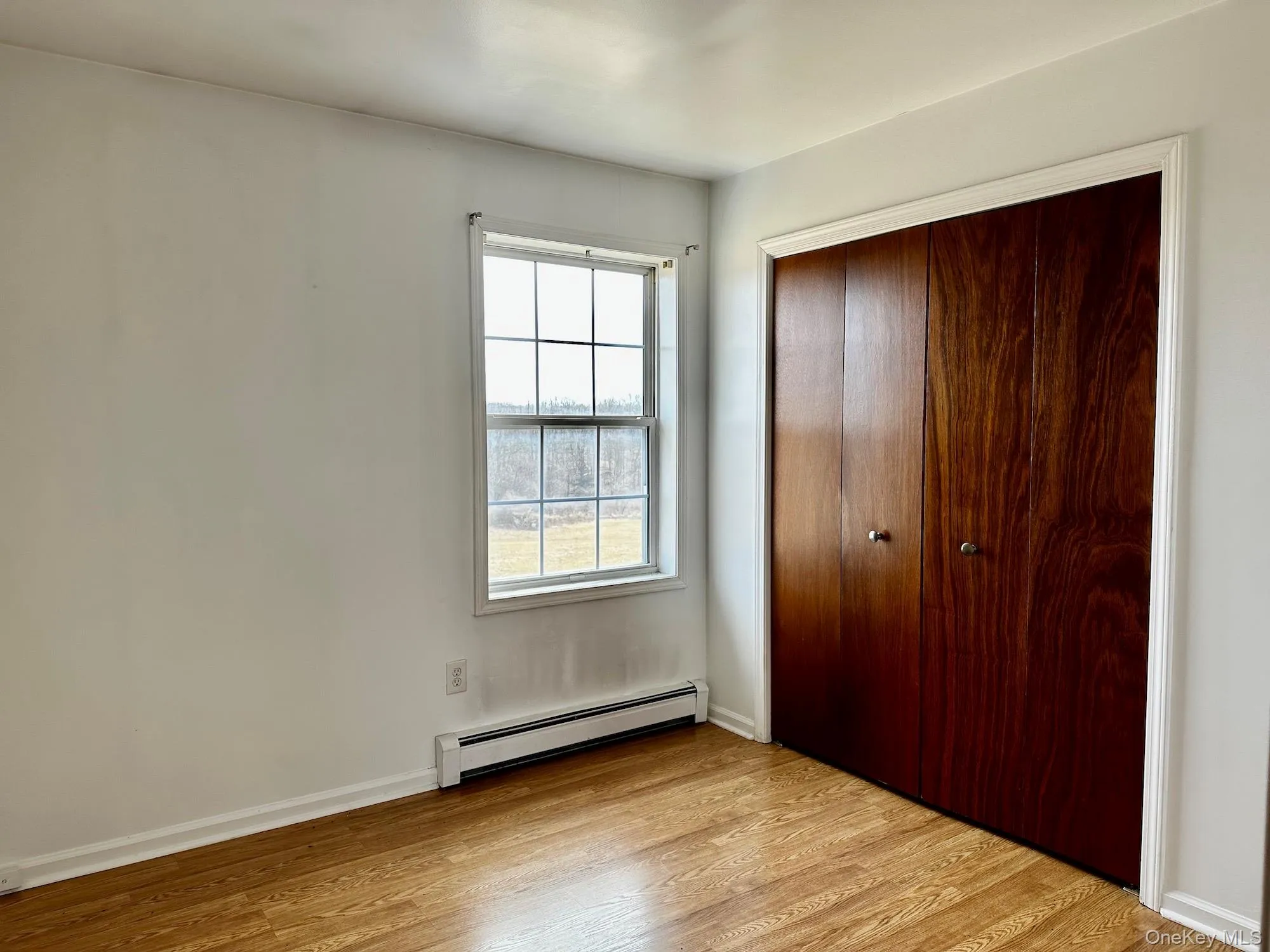 Unfurnished bedroom featuring baseboard heating, light wood-style floors, and a closet Unfurnished bedroom featuring baseboard heating, light wood-style floors, and a closet