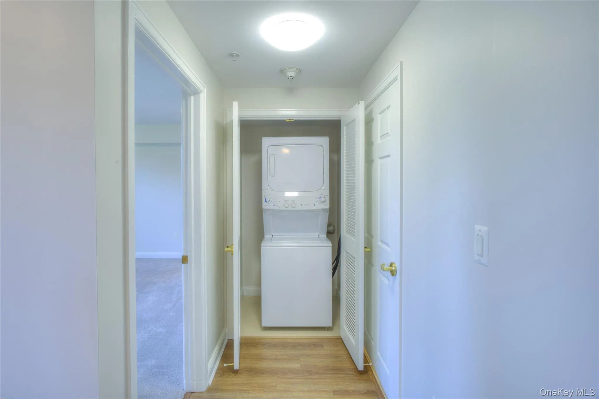 Hall with stacked washer / drying machine and light wood finished floors Hall with stacked washer / drying machine and light wood finished floors