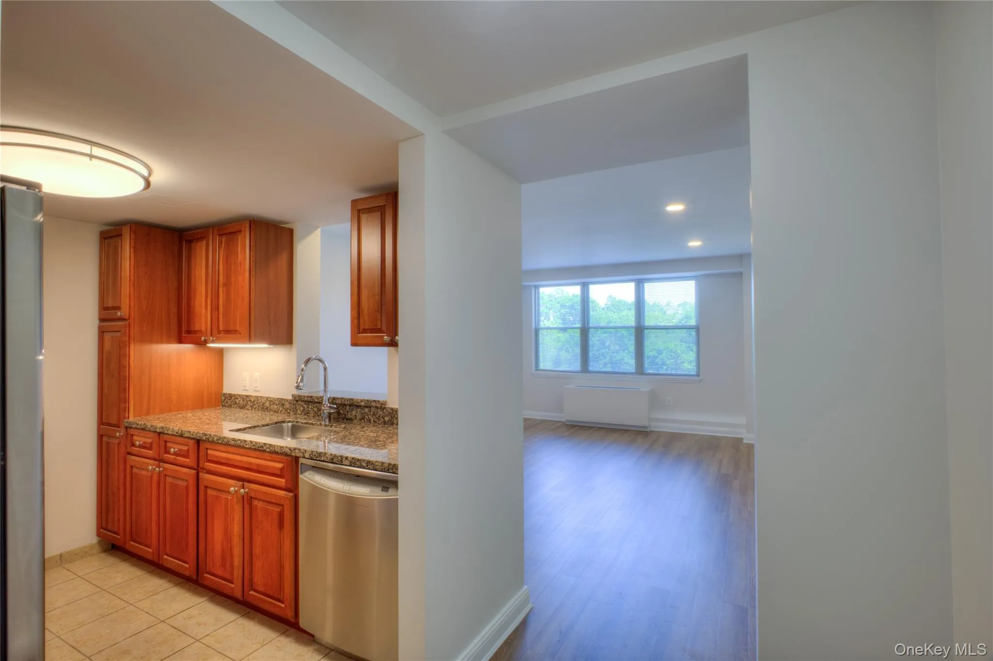 Kitchen featuring stainless steel dishwasher, radiator heating unit, refrigerator, brown cabinetry, and recessed lighting Kitchen featuring stainless steel dishwasher, radiator heating unit, refrigerator, brown cabinetry, and recessed lighting