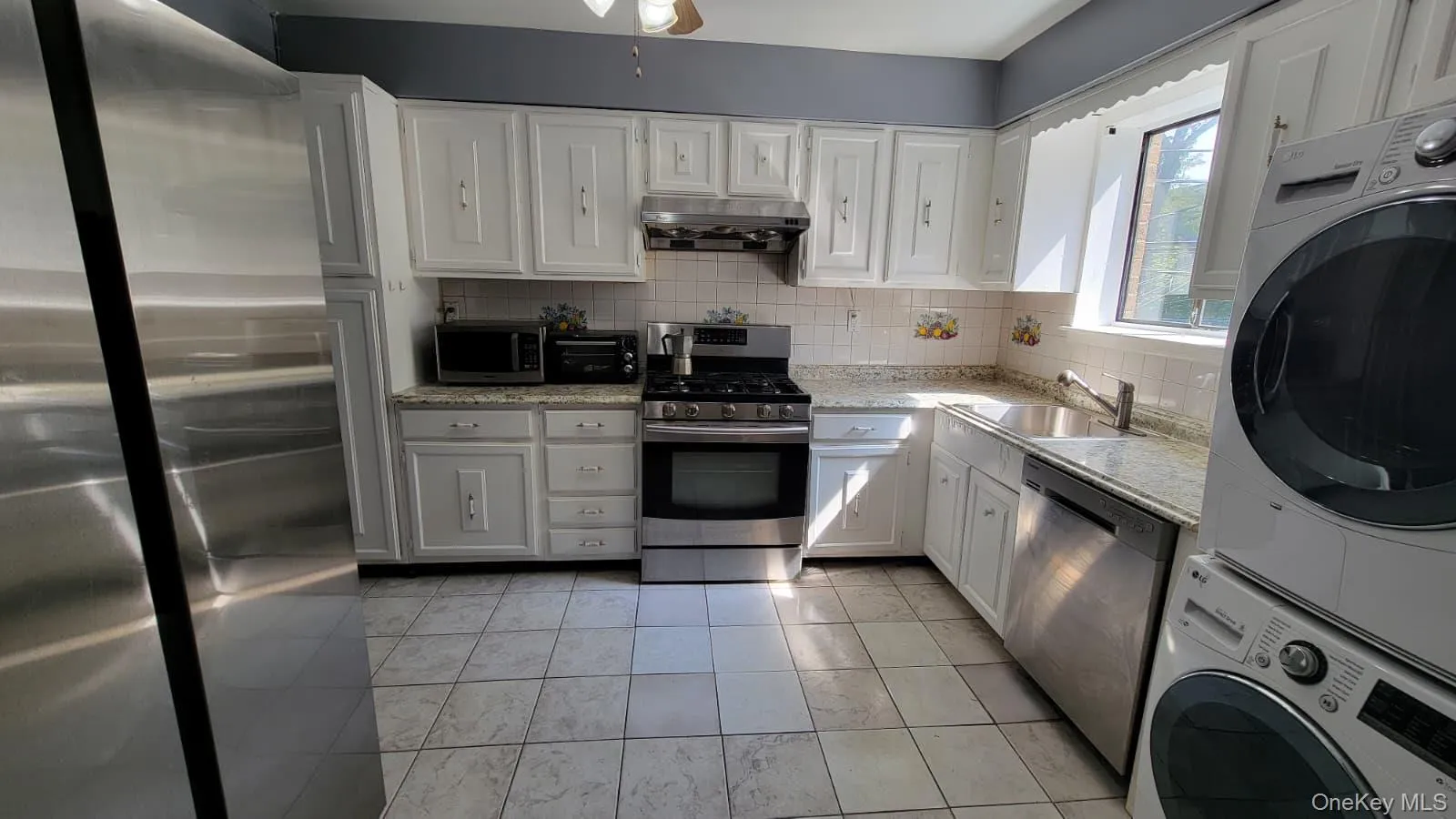 Kitchen featuring stainless steel appliances, backsplash, white cabinetry, under cabinet range hood, and light tile patterned flooring Kitchen featuring stainless steel appliances, backsplash, white cabinetry, under cabinet range hood, and light tile patterned flooring
