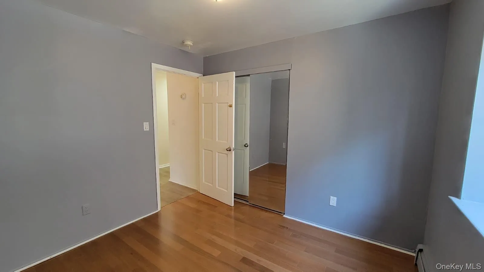 Unfurnished bedroom with wood finished floors, a closet, and a baseboard heating unit Unfurnished bedroom with wood finished floors, a closet, and a baseboard heating unit