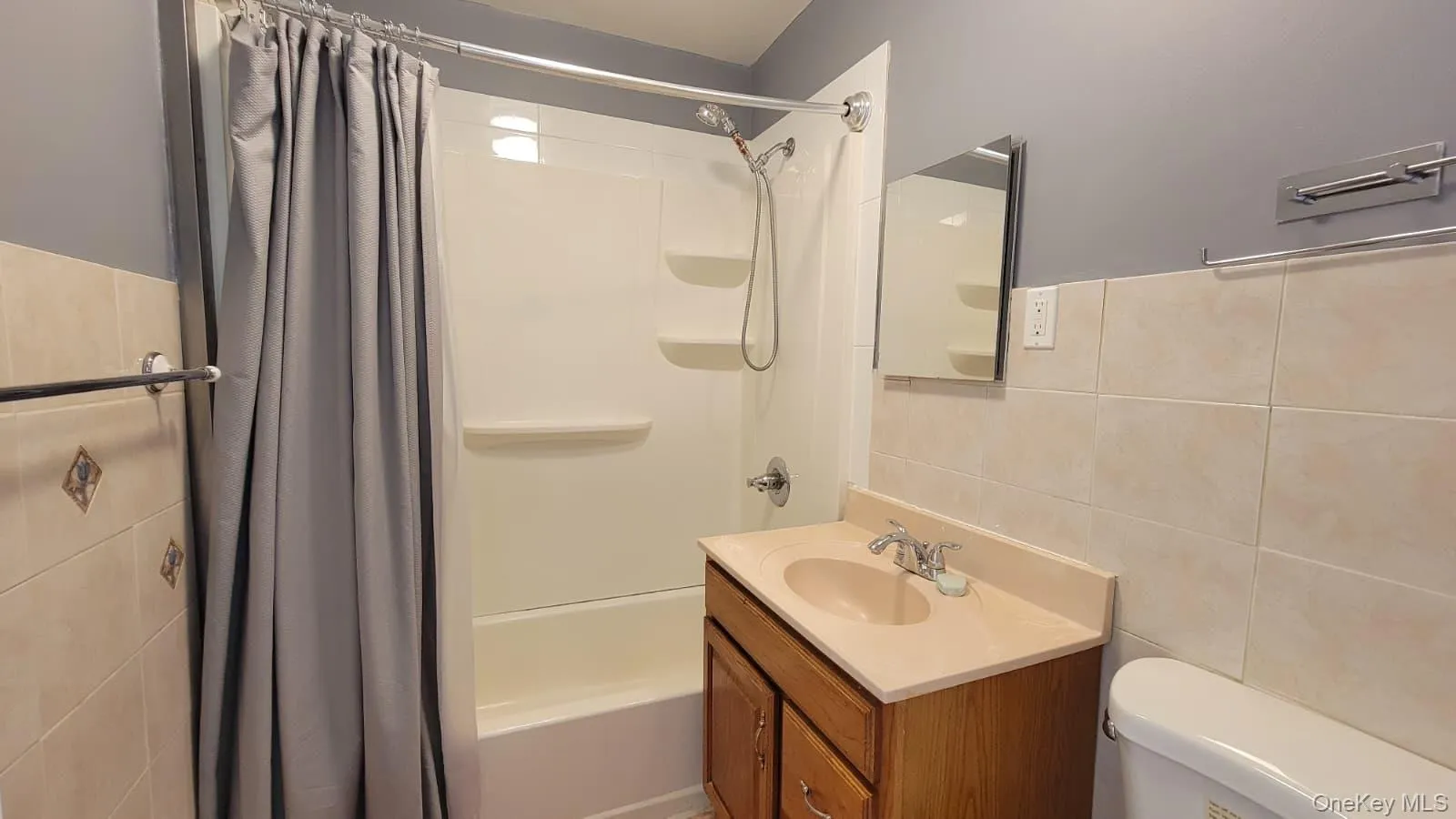 Bathroom featuring tile walls, shower / bath combo with shower curtain, and vanity Bathroom featuring tile walls, shower / bath combo with shower curtain, and vanity