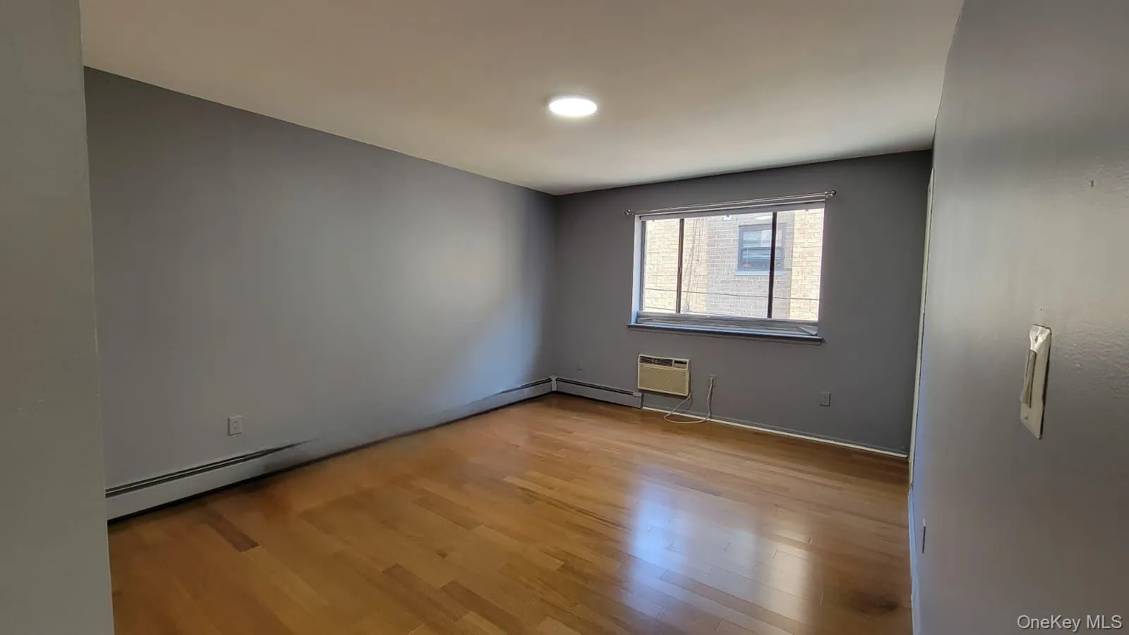 Unfurnished room featuring light wood-style flooring, baseboard heating, and a wall mounted air conditioner Unfurnished room featuring light wood-style flooring, baseboard heating, and a wall mounted air conditioner