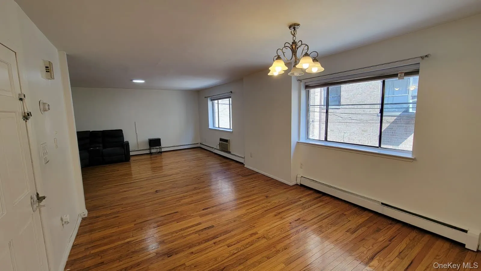 Unfurnished living room with a baseboard radiator, light wood-style flooring, a chandelier, and baseboard heating Unfurnished living room with a baseboard radiator, light wood-style flooring, a chandelier, and baseboard heating