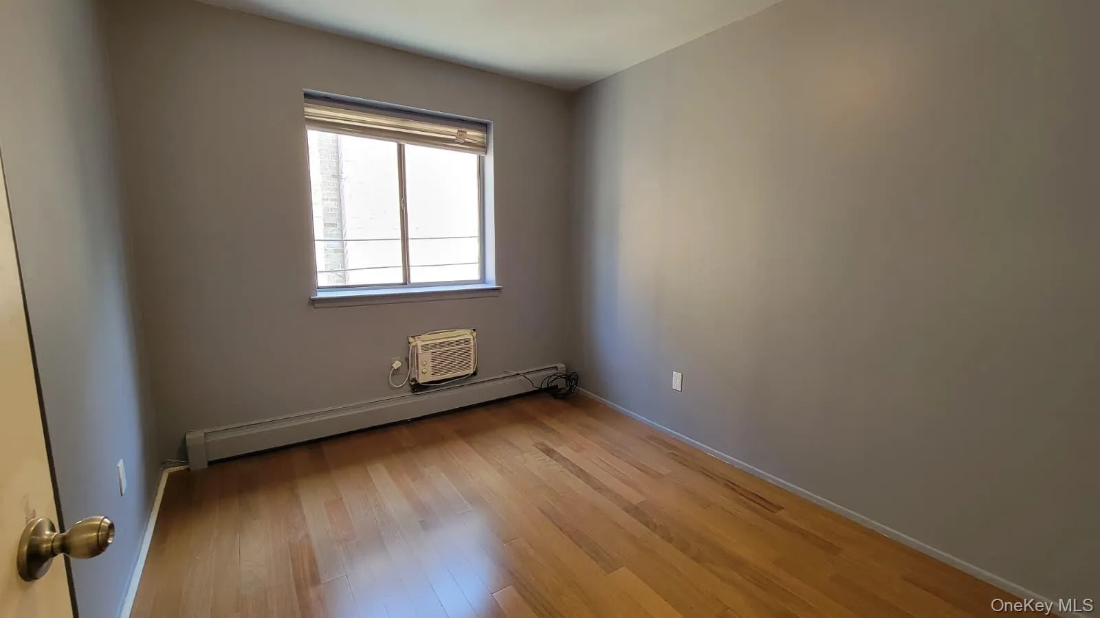 Spare room featuring light wood-style flooring, a baseboard heating unit, and a wall mounted air conditioner Spare room featuring light wood-style flooring, a baseboard heating unit, and a wall mounted air conditioner