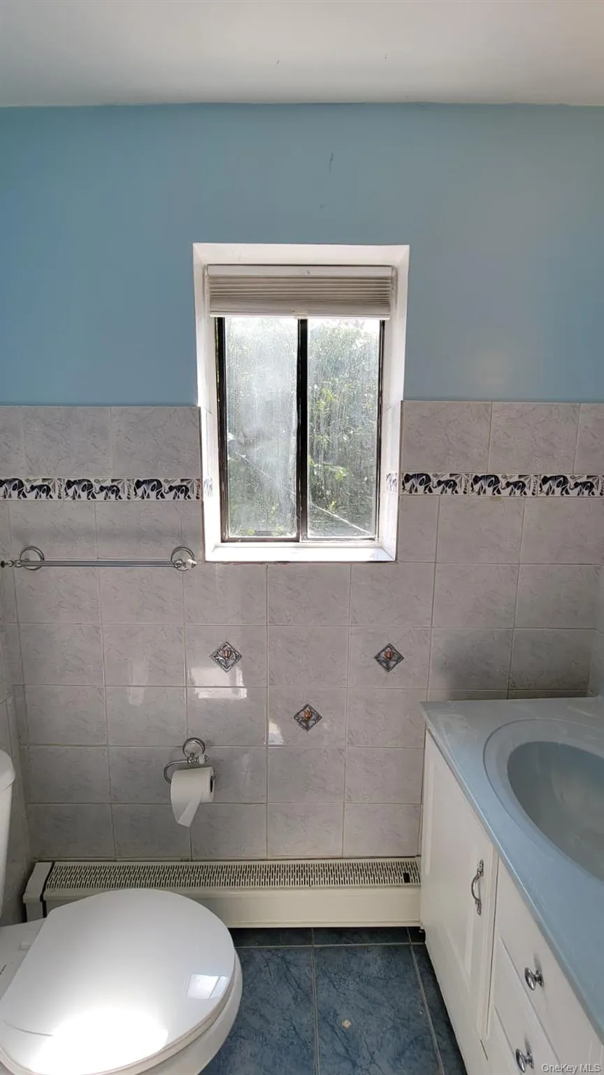 Half bath with vanity, tile walls, a baseboard radiator, a wainscoted wall, and dark tile patterned flooring Half bath with vanity, tile walls, a baseboard radiator, a wainscoted wall, and dark tile patterned flooring