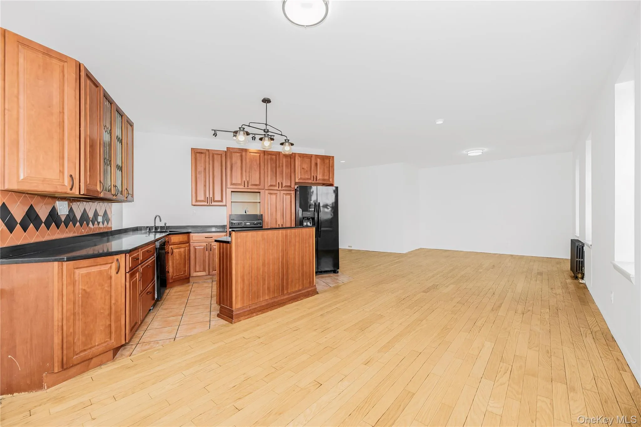 Kitchen featuring dark countertops, decorative backsplash, a center island, black appliances, and brown cabinets Kitchen featuring dark countertops, decorative backsplash, a center island, black appliances, and brown cabinets