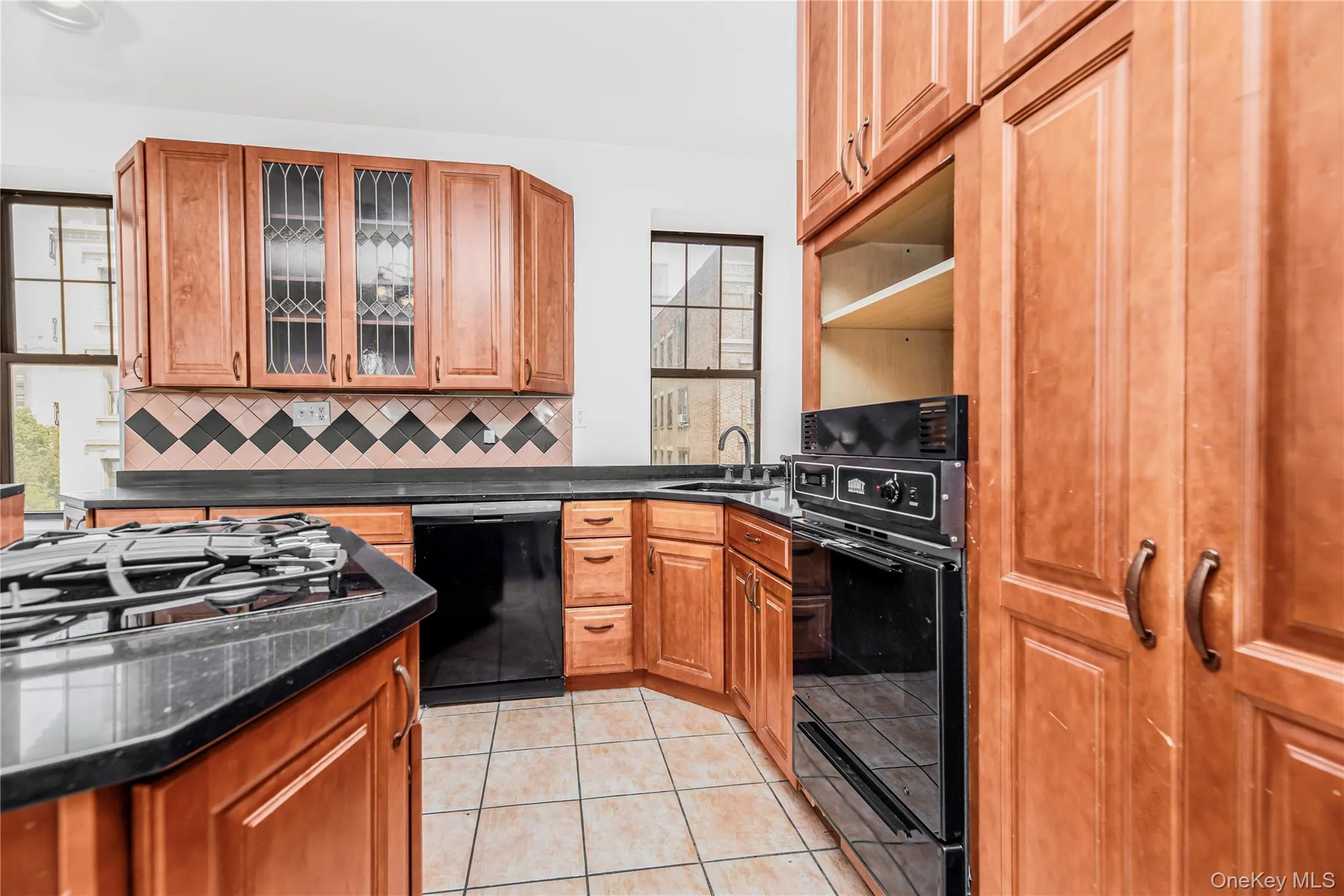 Kitchen with light tile patterned flooring, tasteful backsplash, black appliances, and brown cabinets Kitchen with light tile patterned flooring, tasteful backsplash, black appliances, and brown cabinets