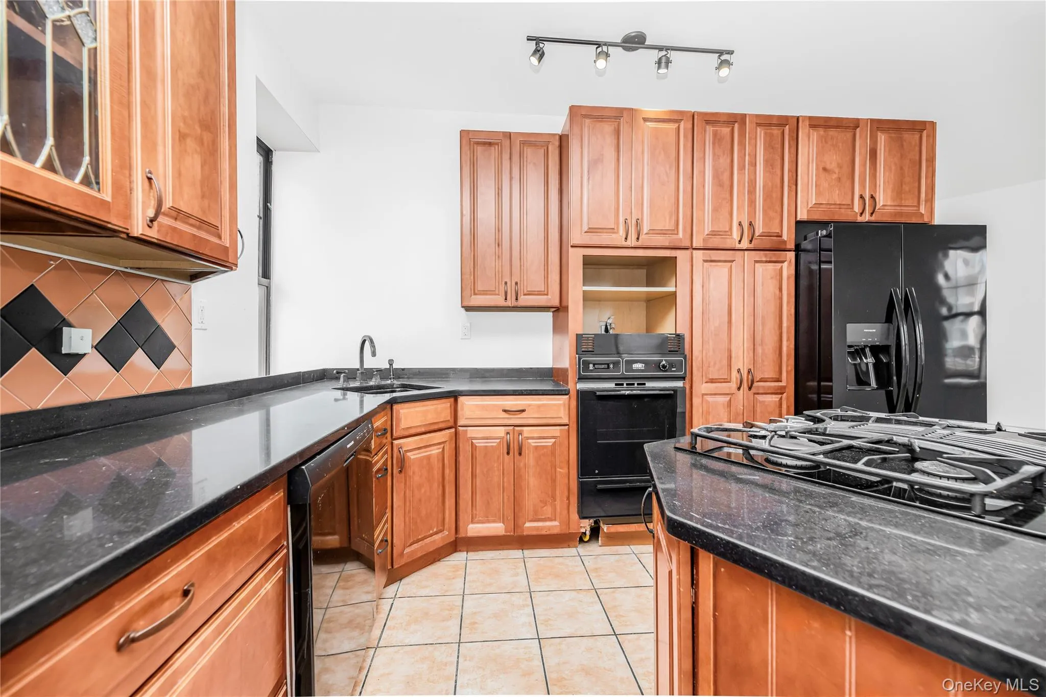 Kitchen with black appliances, light tile patterned flooring, tasteful backsplash, and brown cabinets Kitchen with black appliances, light tile patterned flooring, tasteful backsplash, and brown cabinets