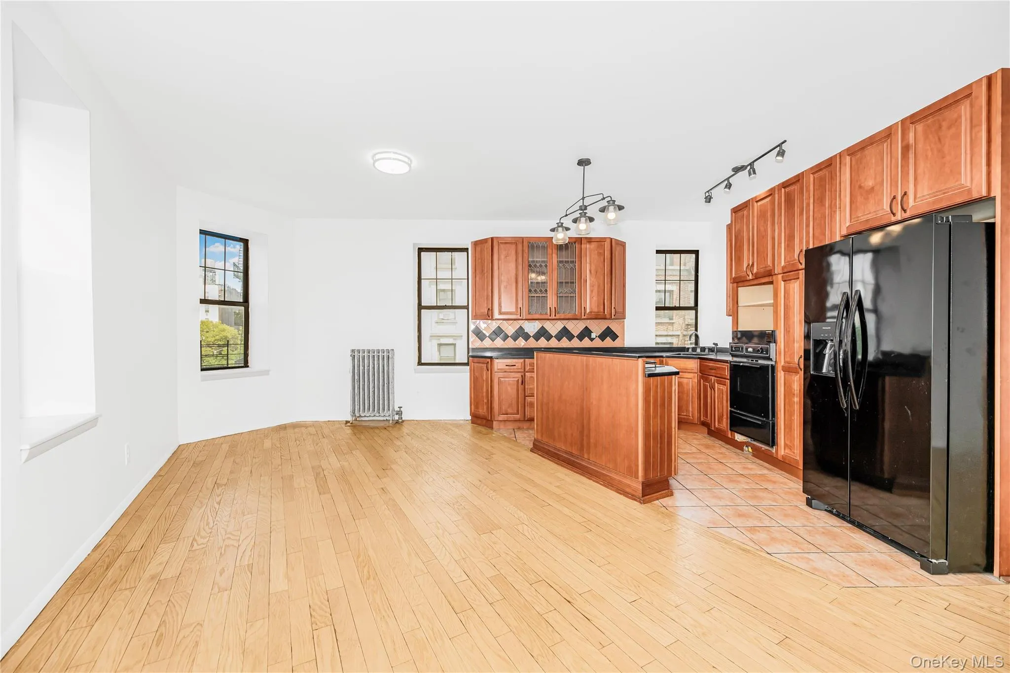 Kitchen featuring black appliances, decorative backsplash, a kitchen island, brown cabinetry, and radiator heating unit Kitchen featuring black appliances, decorative backsplash, a kitchen island, brown cabinetry, and radiator heating unit