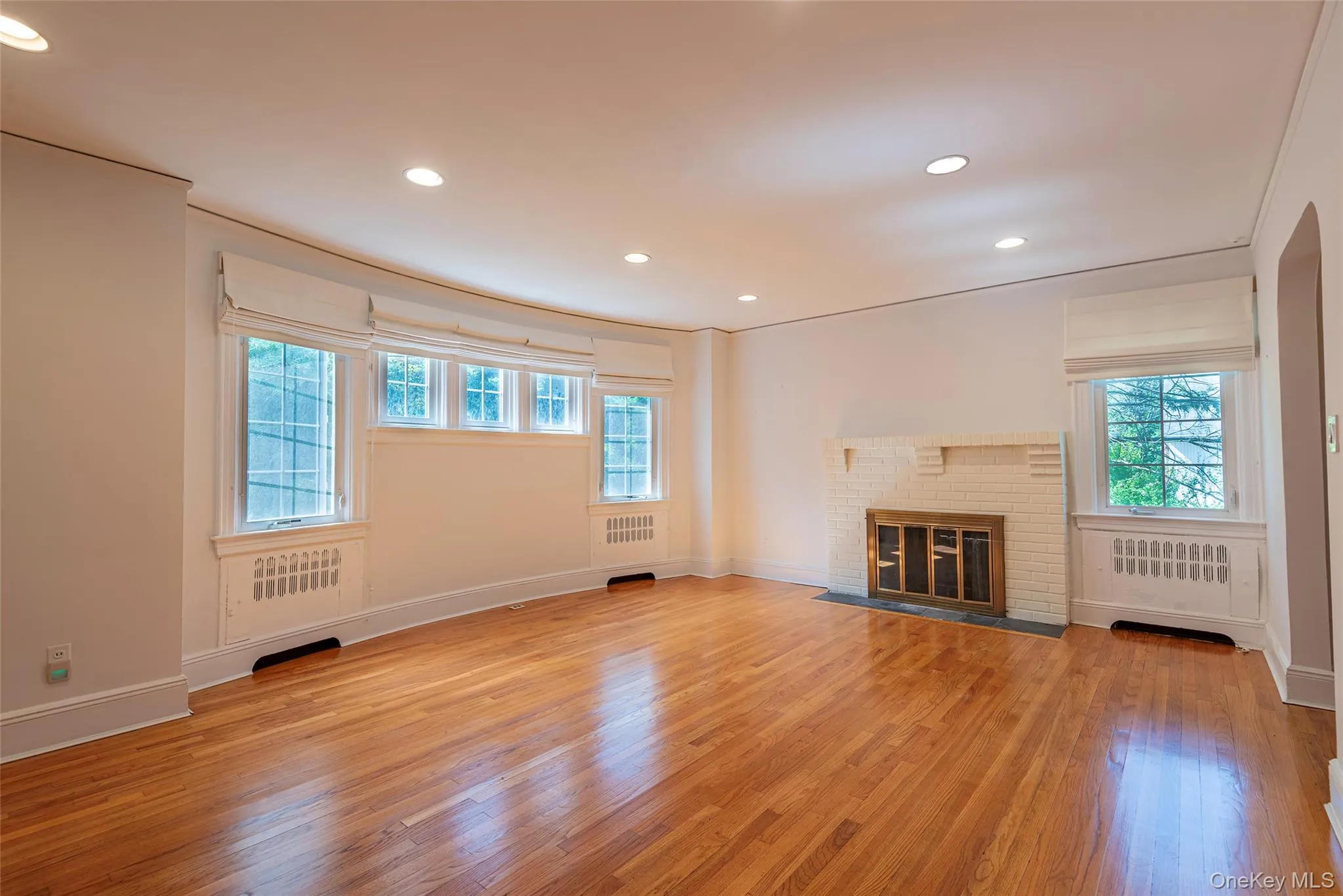 Unfurnished living room with light wood-style flooring, recessed lighting, a fireplace, and radiator heating unit Unfurnished living room with light wood-style flooring, recessed lighting, a fireplace, and radiator heating unit