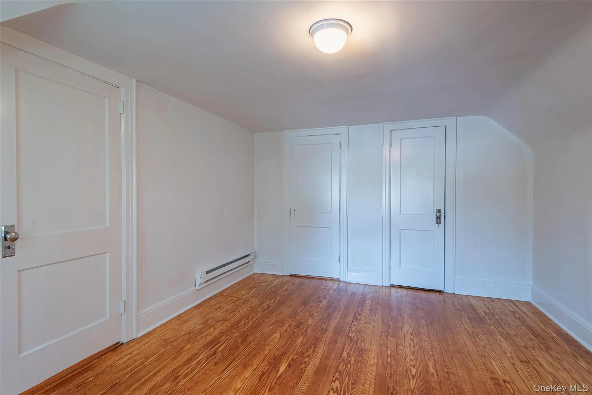 Unfurnished bedroom featuring light wood finished floors, a baseboard heating unit, and two closets Unfurnished bedroom featuring light wood finished floors, a baseboard heating unit, and two closets