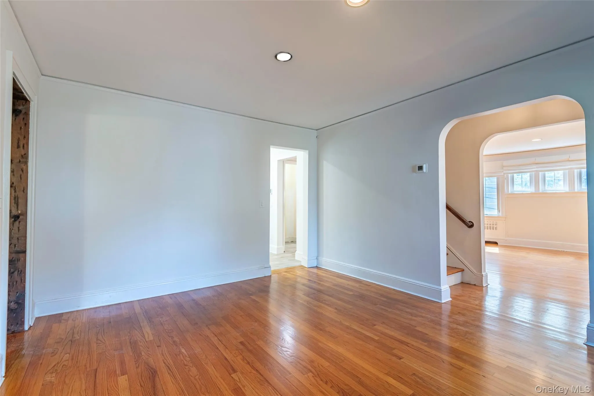 Spare room featuring light wood-style floors, arched walkways, recessed lighting, and stairs Spare room featuring light wood-style floors, arched walkways, recessed lighting, and stairs