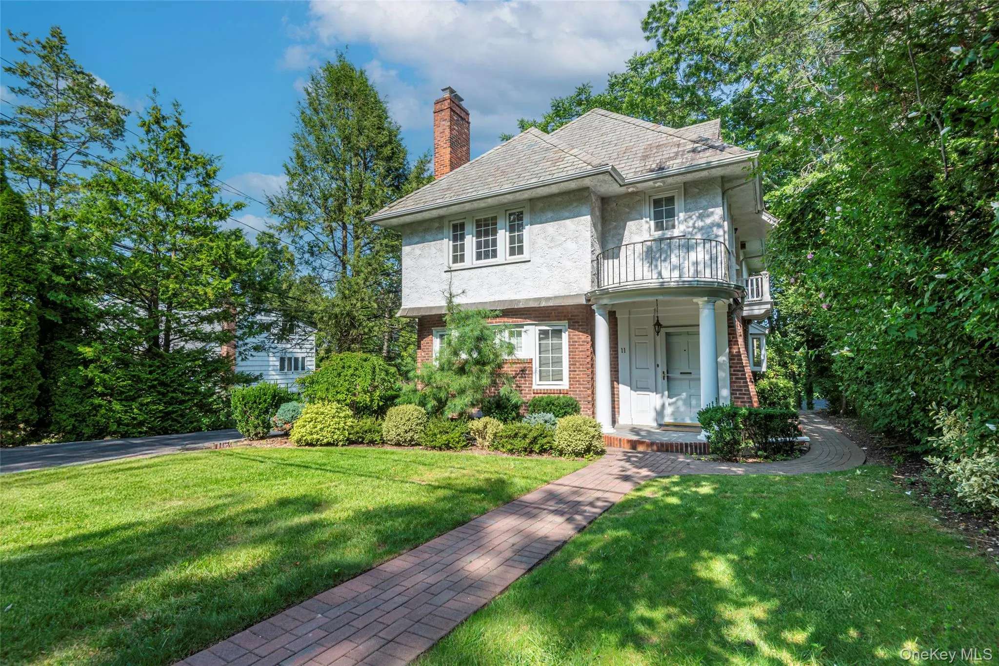 View of front of home featuring a front lawn, brick siding, a balcony, a chimney, and a high end roof View of front of home featuring a front lawn, brick siding, a balcony, a chimney, and a high end roof