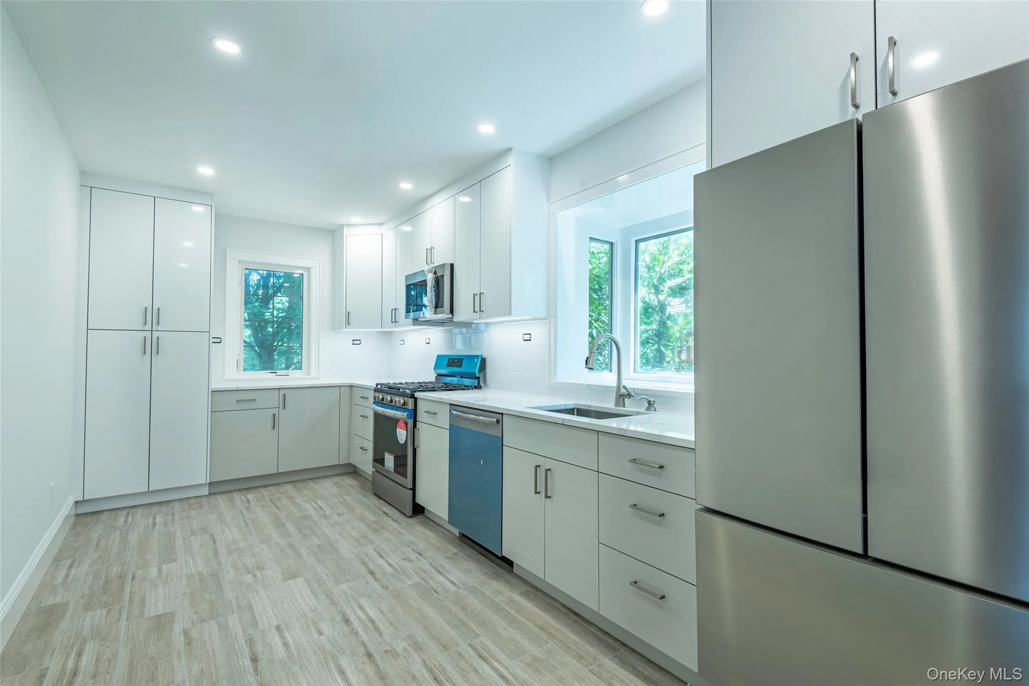 Kitchen featuring stainless steel appliances, plenty of natural light, white cabinetry, light wood-style flooring, and recessed lighting Kitchen featuring stainless steel appliances, plenty of natural light, white cabinetry, light wood-style flooring, and recessed lighting