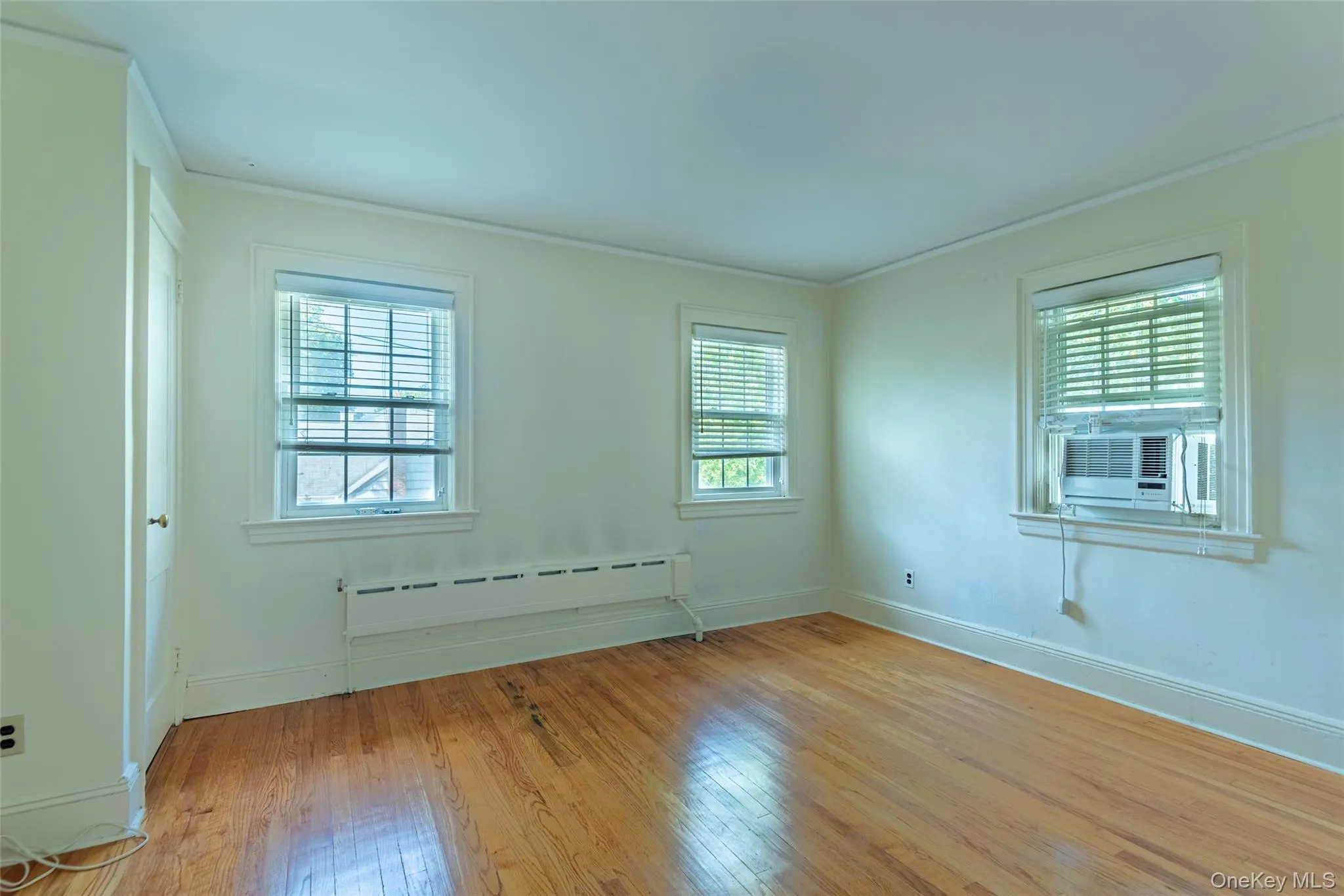 Spare room featuring light wood-style floors, baseboard heating, ornamental molding, and cooling unit Spare room featuring light wood-style floors, baseboard heating, ornamental molding, and cooling unit