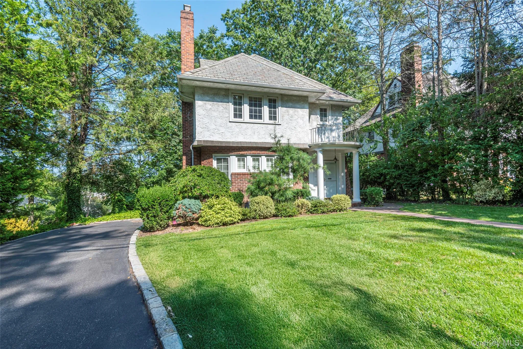 View of front of house featuring brick siding, a front lawn, a balcony, a chimney, and a high end roof View of front of house featuring brick siding, a front lawn, a balcony, a chimney, and a high end roof