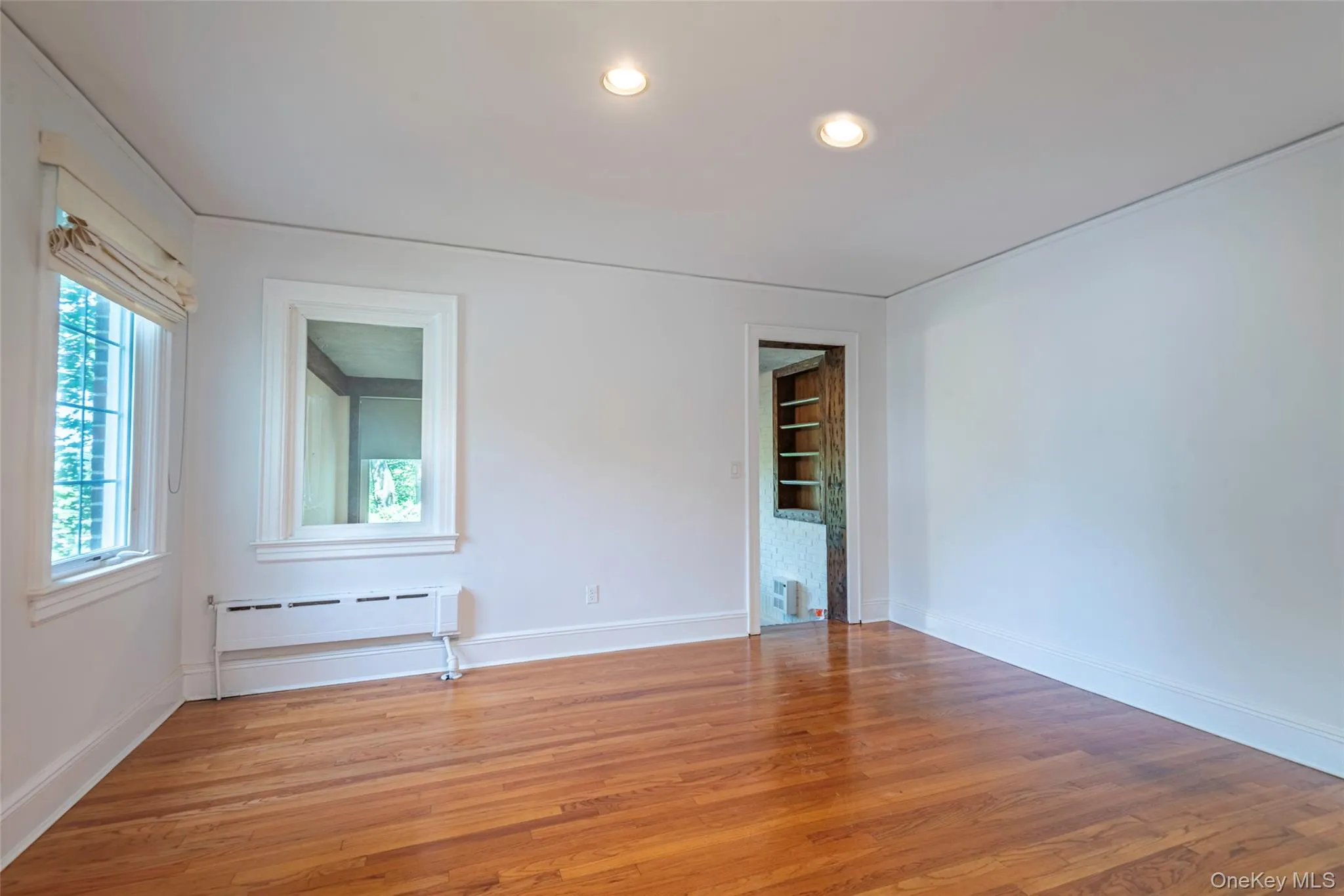 Unfurnished room with recessed lighting, light wood-type flooring, a baseboard radiator, and built in features Unfurnished room with recessed lighting, light wood-type flooring, a baseboard radiator, and built in features