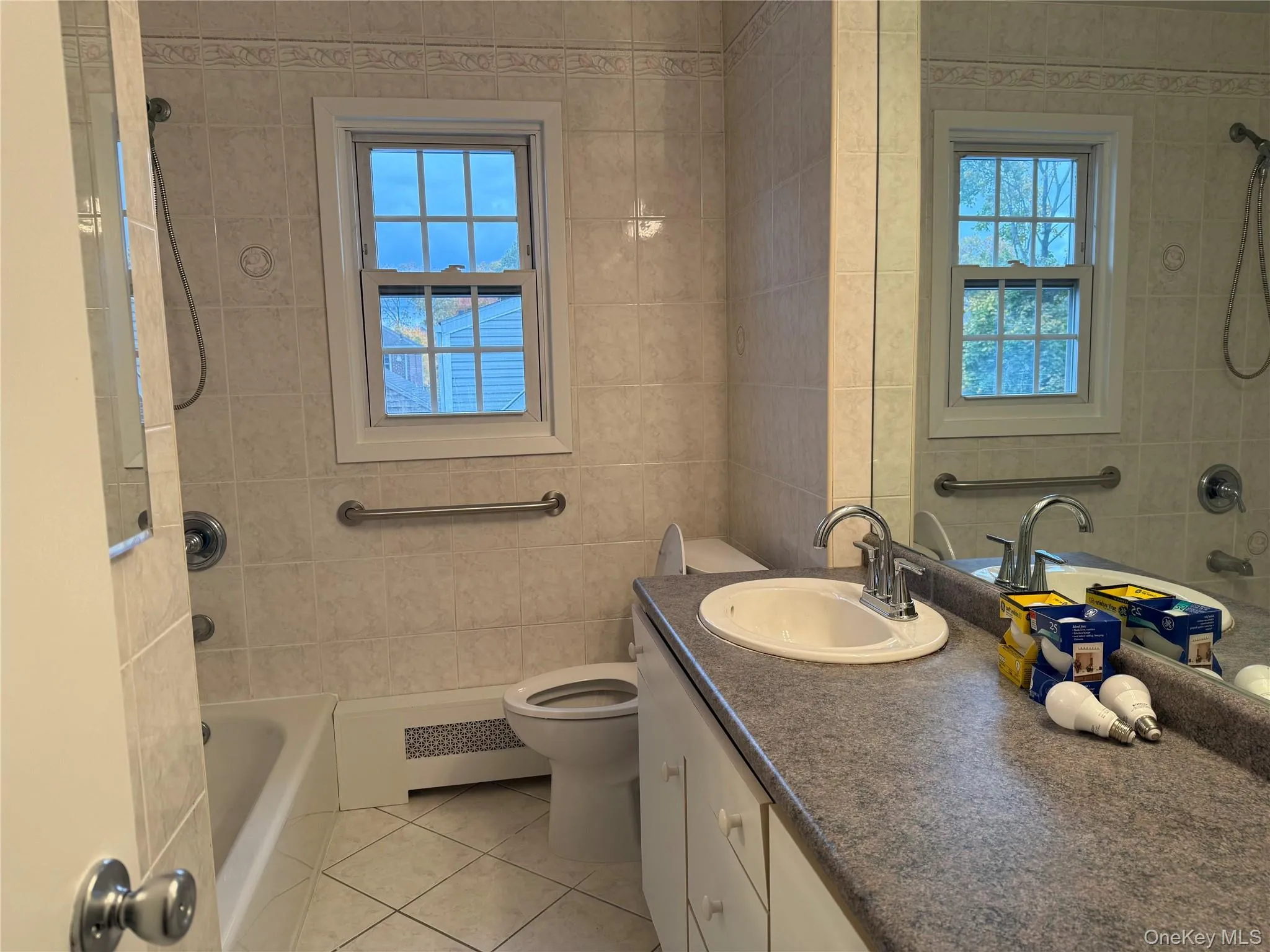 Full bath featuring shower / bathtub combination, healthy amount of natural light, vanity, tile walls, and radiator Full bath featuring shower / bathtub combination, healthy amount of natural light, vanity, tile walls, and radiator